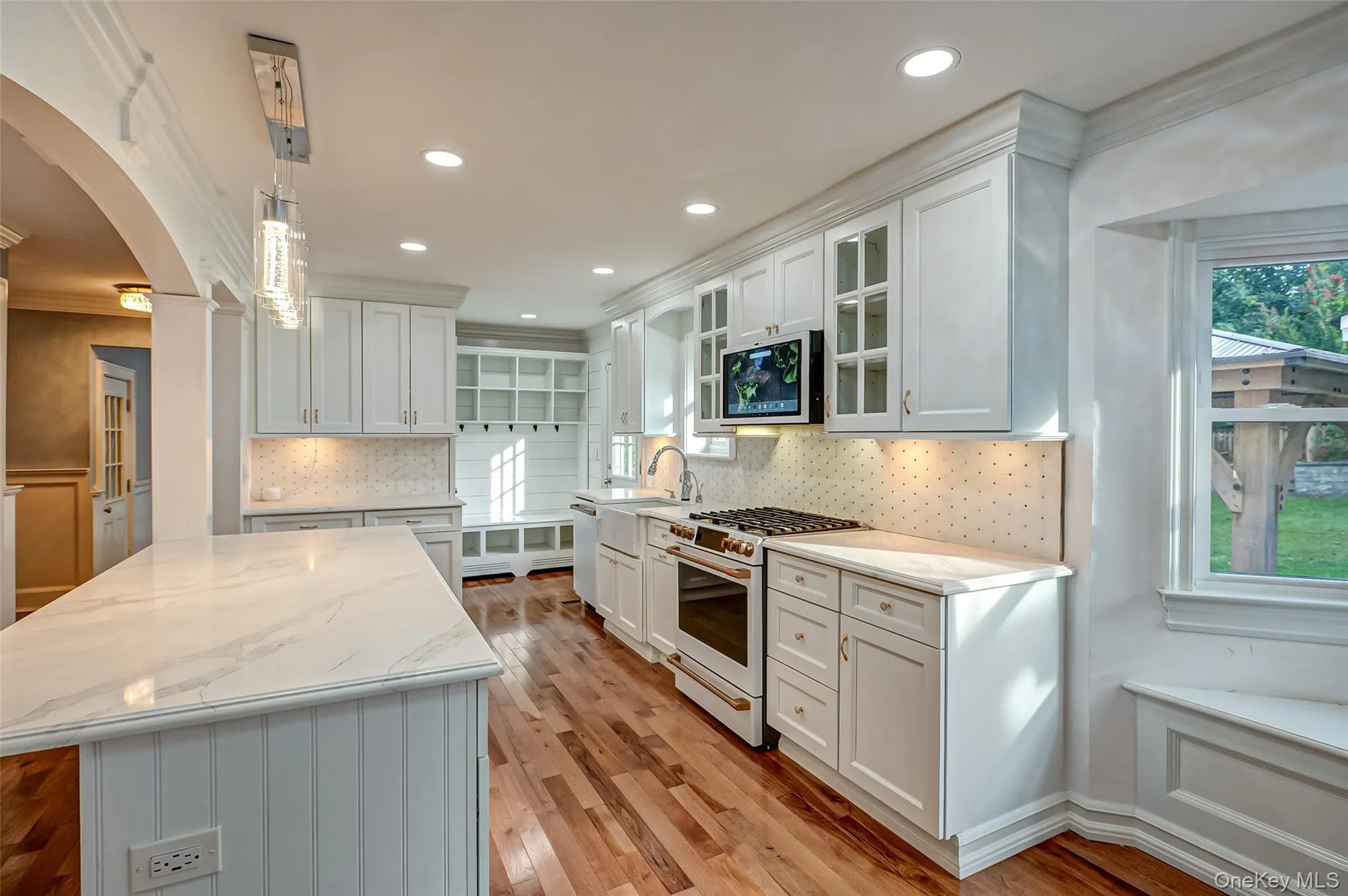 Kitchen with white cabinets, white range with gas stovetop, arched walkways, hanging light fixtures, and marble countertop. Kitchen with white cabinets, white range with gas stovetop, arched walkways, hanging light fixtures, and marble countertop.