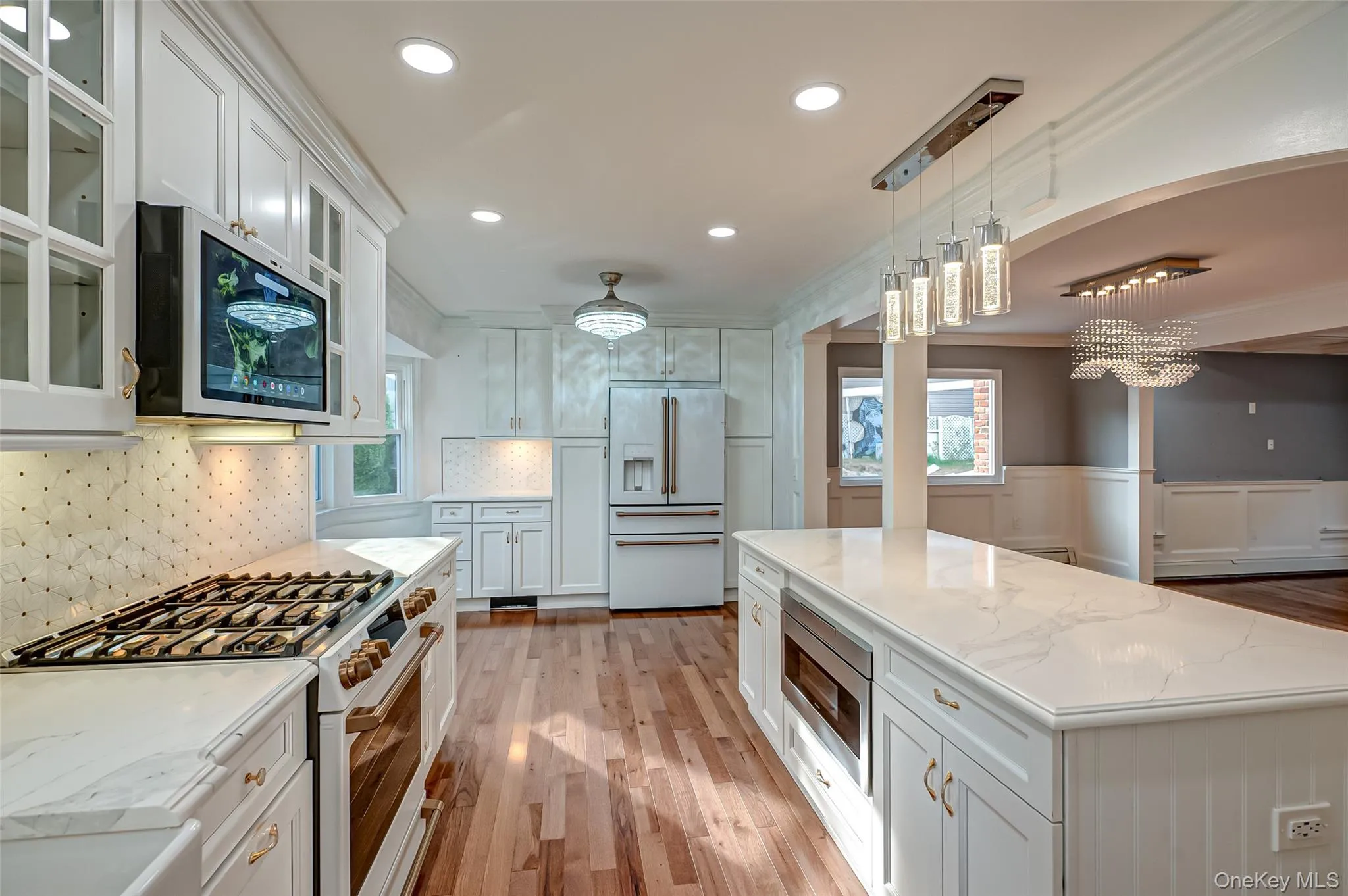 Kitchen with white appliances, white cabinets, decorative light fixtures, a wainscoted wall, and glass insert cabinets Kitchen with white appliances, white cabinets, decorative light fixtures, a wainscoted wall, and glass insert cabinets