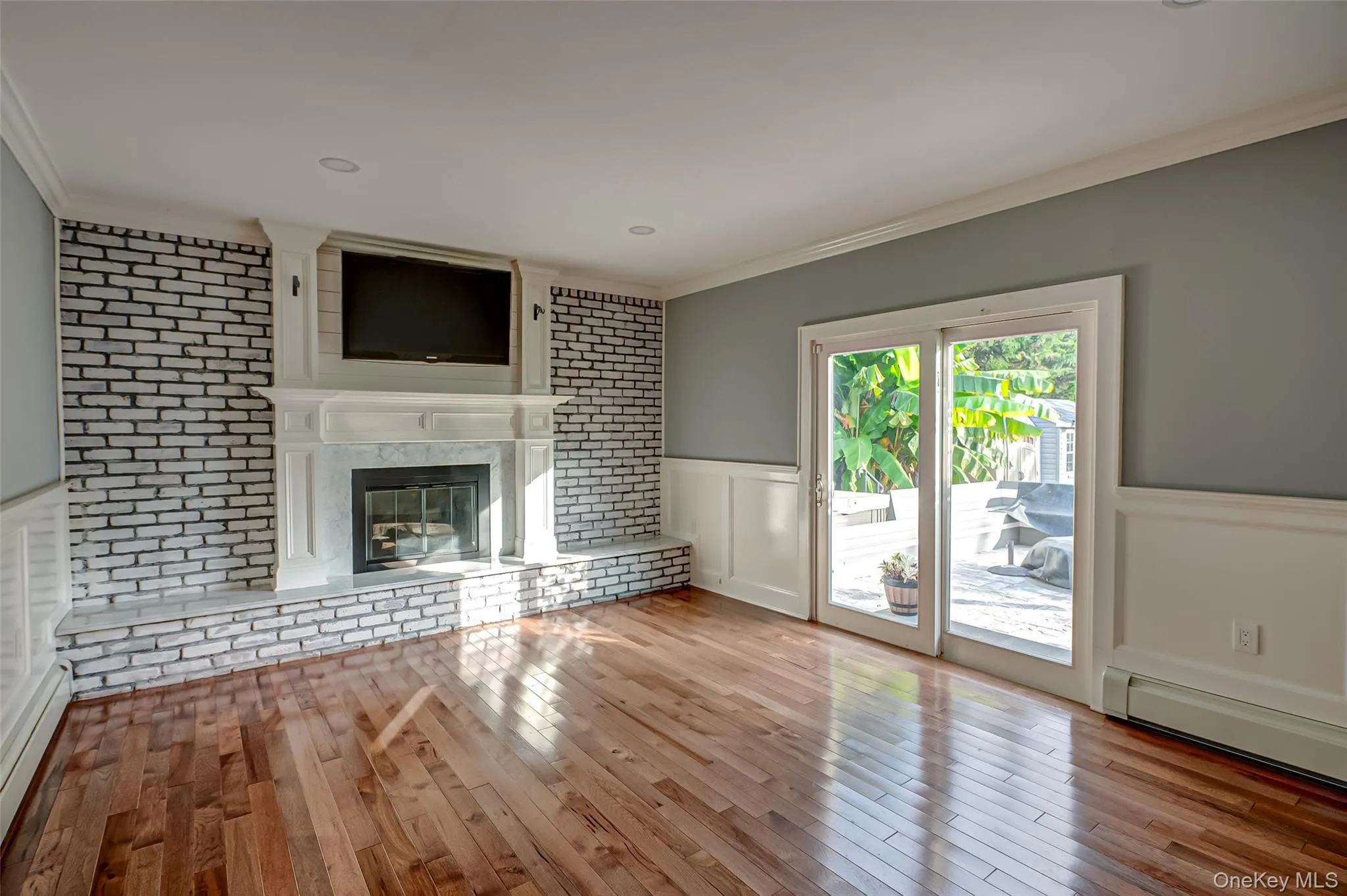 Unfurnished living room featuring a wainscoted wall, a decorative wall, crown molding, a baseboard heating unit, and hardwood / wood-style flooring Unfurnished living room featuring a wainscoted wall, a decorative wall, crown molding, a baseboard heating unit, and hardwood / wood-style flooring
