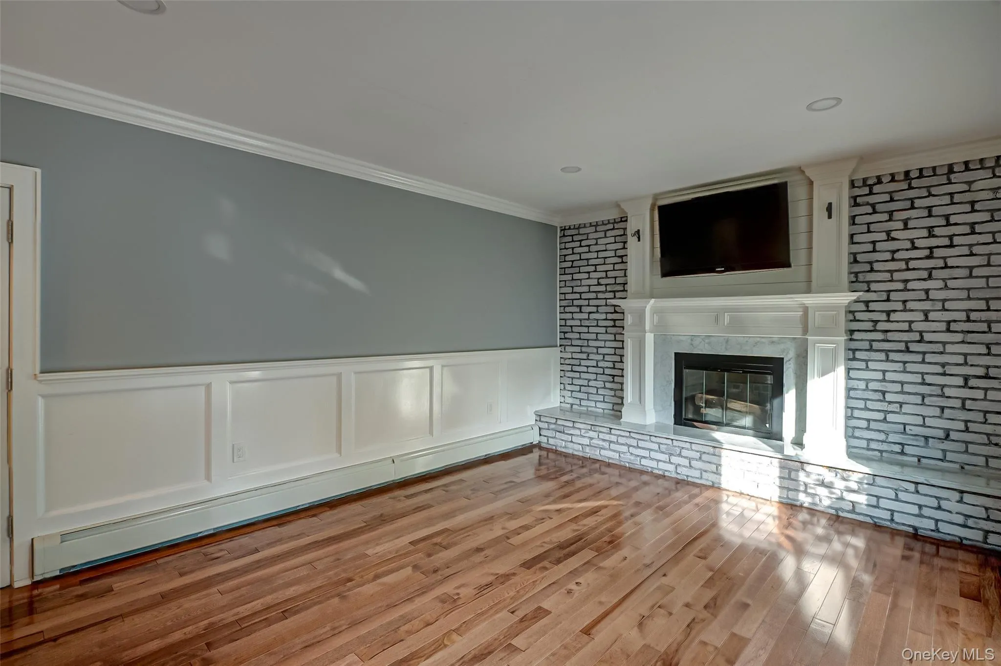 Unfurnished living room with wainscoting, a decorative wall, a baseboard radiator, ornamental molding, and a high end fireplace Unfurnished living room with wainscoting, a decorative wall, a baseboard radiator, ornamental molding, and a high end fireplace