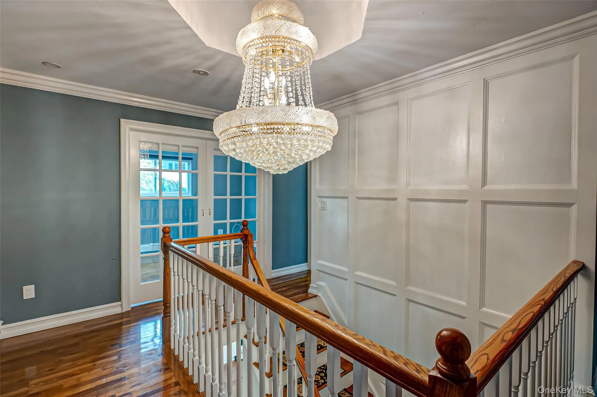 Corridor featuring an upstairs landing, office with french glass doors, a chandelier, crown molding, wood flooring. Corridor featuring an upstairs landing, office with french glass doors, a chandelier, crown molding, wood flooring.