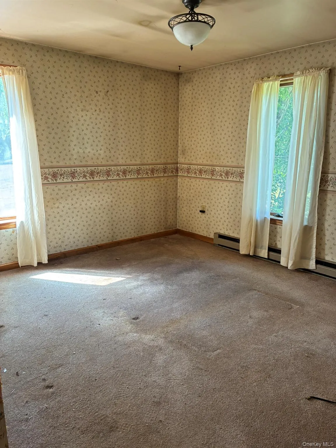Carpeted empty room with healthy amount of natural light, a baseboard radiator, and wallpapered walls Carpeted empty room with healthy amount of natural light, a baseboard radiator, and wallpapered walls