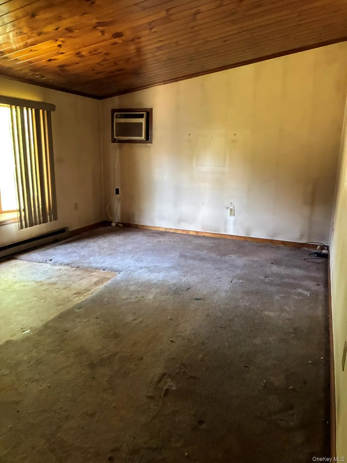 Carpeted empty room with wooden ceiling, baseboard heating, and a wall unit AC Carpeted empty room with wooden ceiling, baseboard heating, and a wall unit AC