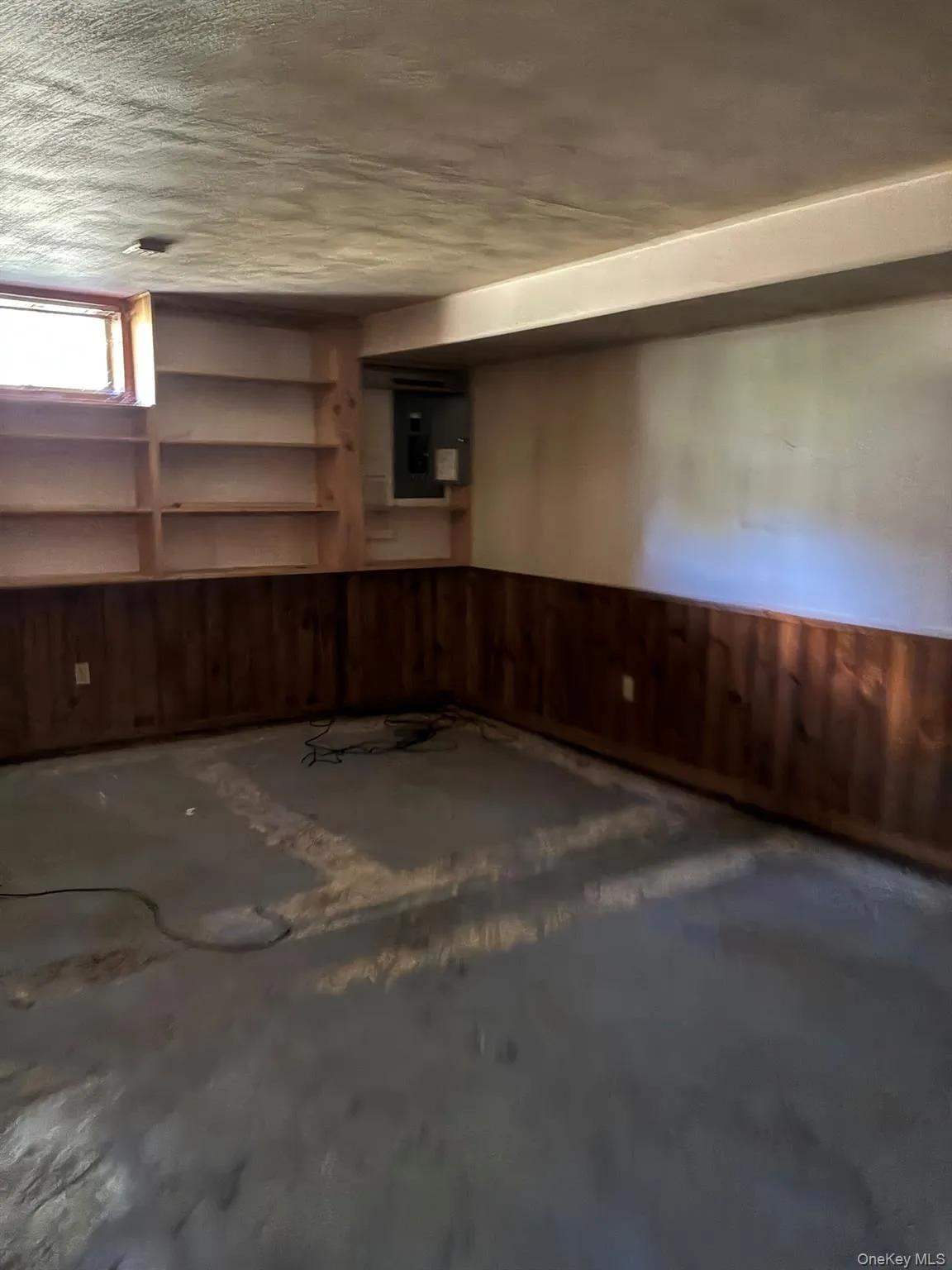 Below grade area with wood walls, a wainscoted wall, electric panel, and a textured ceiling Below grade area with wood walls, a wainscoted wall, electric panel, and a textured ceiling