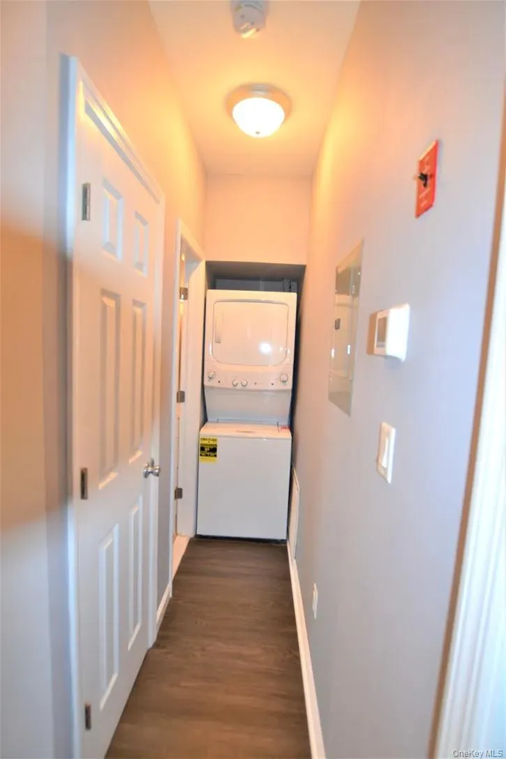 Corridor with stacked washer / dryer, dark wood-style floors, and electric panel Corridor with stacked washer / dryer, dark wood-style floors, and electric panel