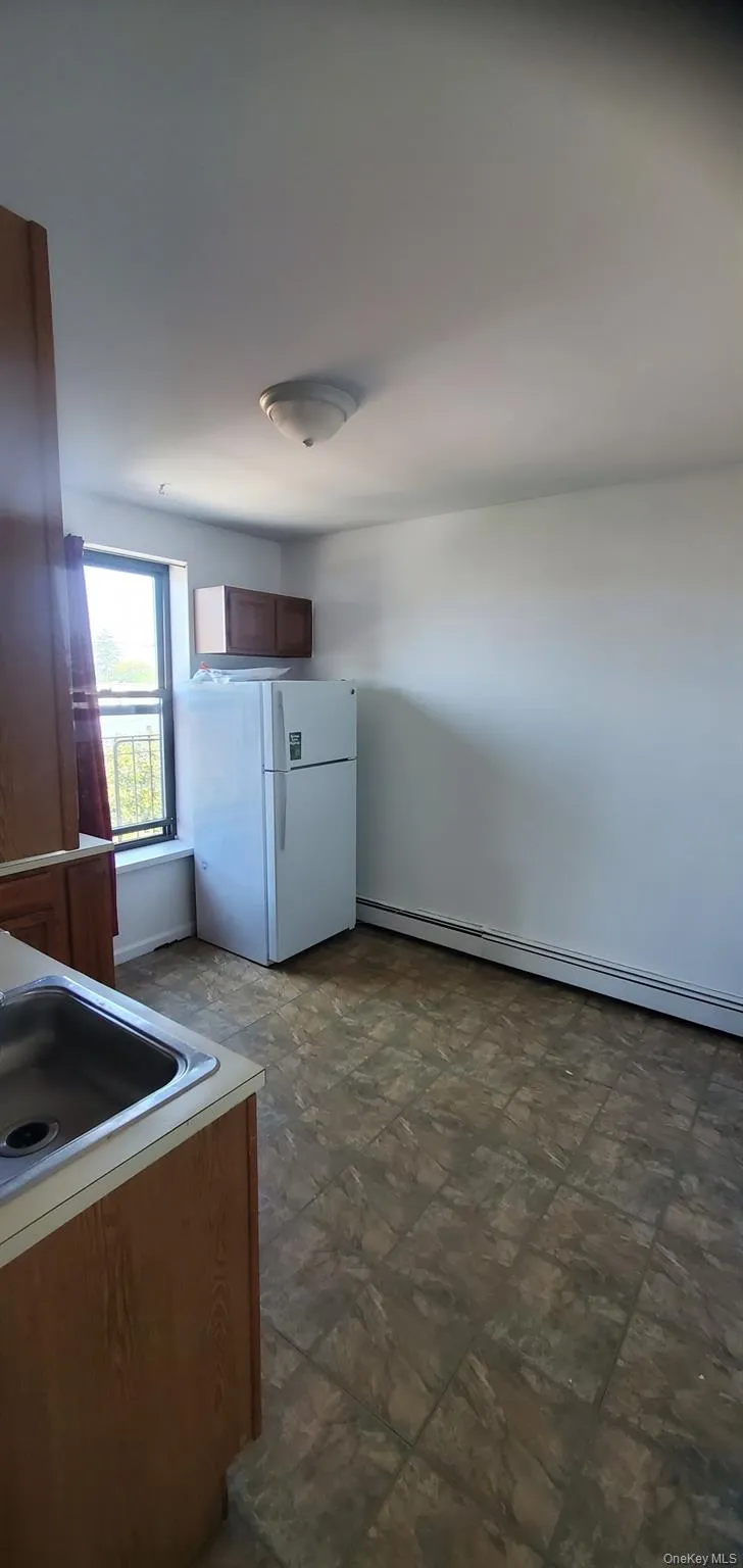 Kitchen with freestanding refrigerator, brown cabinets, a baseboard radiator, and light countertops Kitchen with freestanding refrigerator, brown cabinets, a baseboard radiator, and light countertops