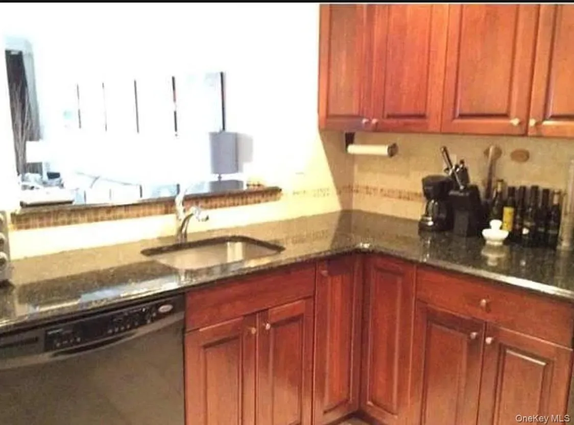 Kitchen with dishwasher, brown cabinets, and dark stone counters Kitchen with dishwasher, brown cabinets, and dark stone counters
