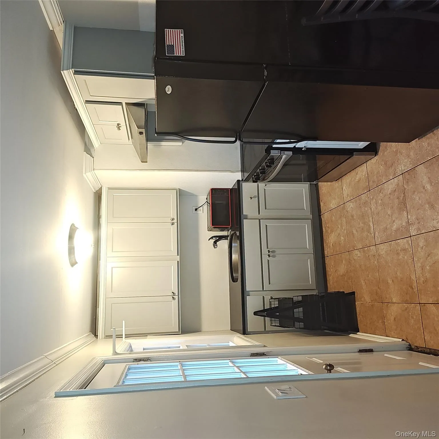 Kitchen with fridge, dark countertops, stove, ventilation hood, and light tile patterned floors Kitchen with fridge, dark countertops, stove, ventilation hood, and light tile patterned floors