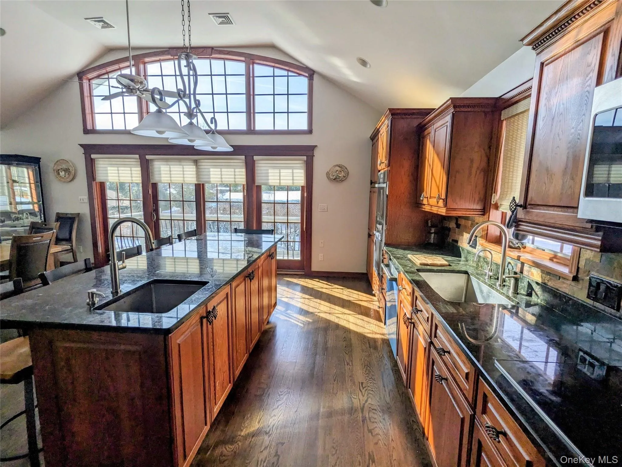 Kitchen with a kitchen breakfast bar, decorative light fixtures, brown cabinetry, a center island with sink, and high vaulted ceiling Kitchen with a kitchen breakfast bar, decorative light fixtures, brown cabinetry, a center island with sink, and high vaulted ceiling