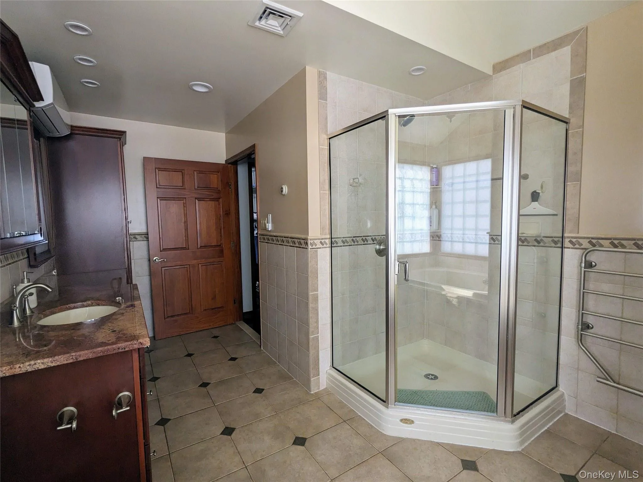 Bathroom with vanity, light tile patterned floors, a shower stall, tile walls, and a wainscoted wall Bathroom with vanity, light tile patterned floors, a shower stall, tile walls, and a wainscoted wall