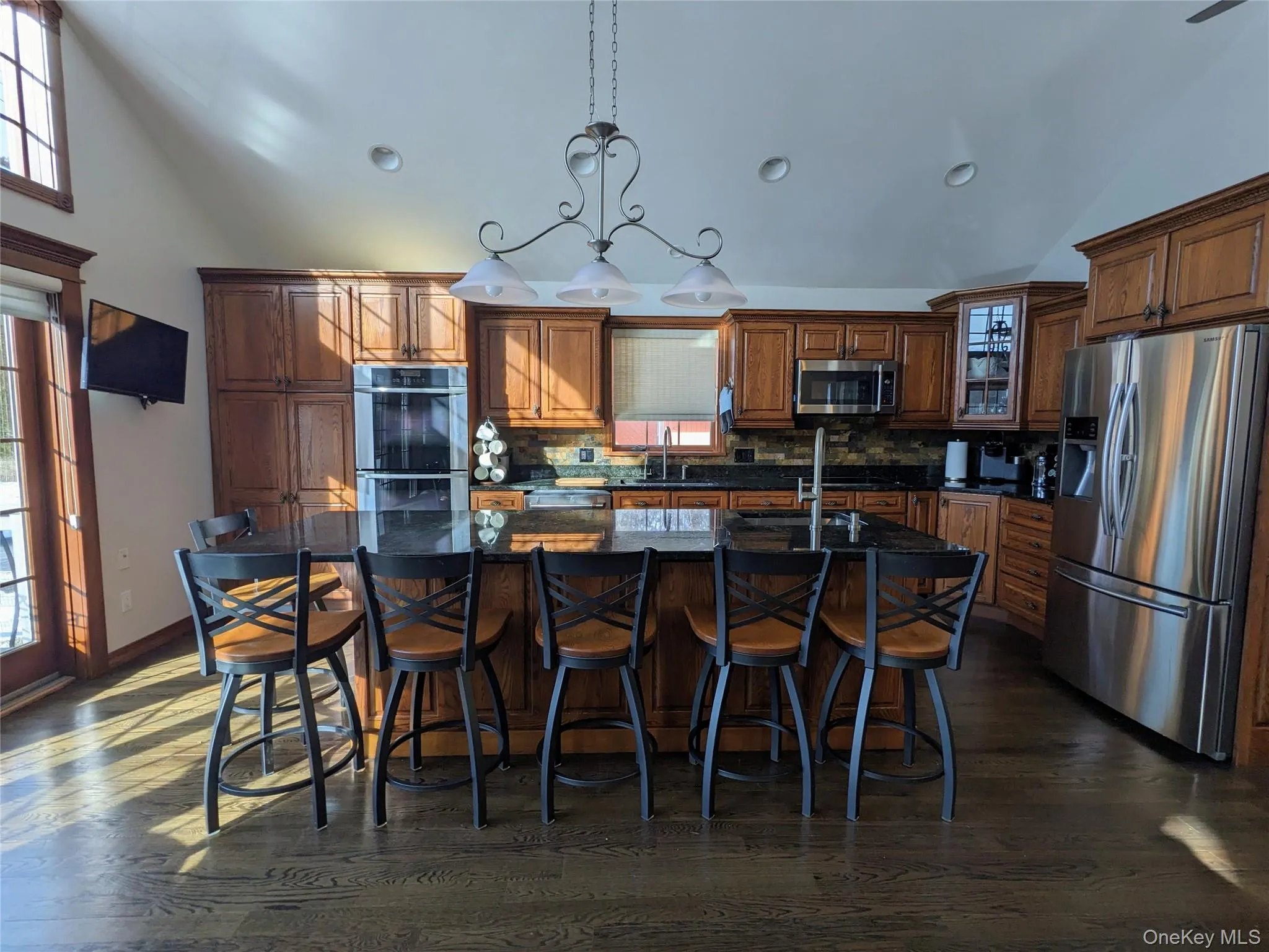 Kitchen featuring appliances with stainless steel finishes, backsplash, a kitchen island with sink, hanging light fixtures, and a breakfast bar Kitchen featuring appliances with stainless steel finishes, backsplash, a kitchen island with sink, hanging light fixtures, and a breakfast bar