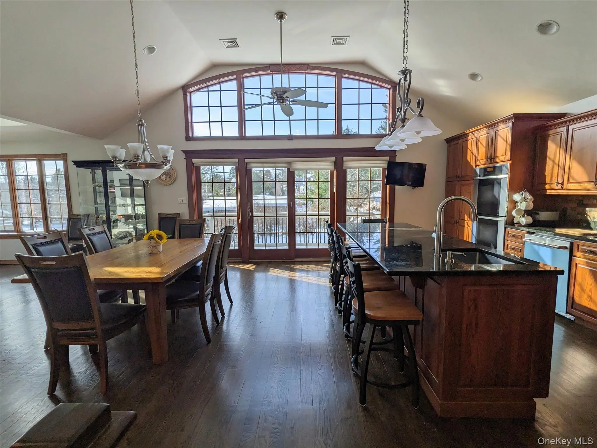 Dining space with a chandelier, dark wood-type flooring, high vaulted ceiling, and ceiling fan Dining space with a chandelier, dark wood-type flooring, high vaulted ceiling, and ceiling fan