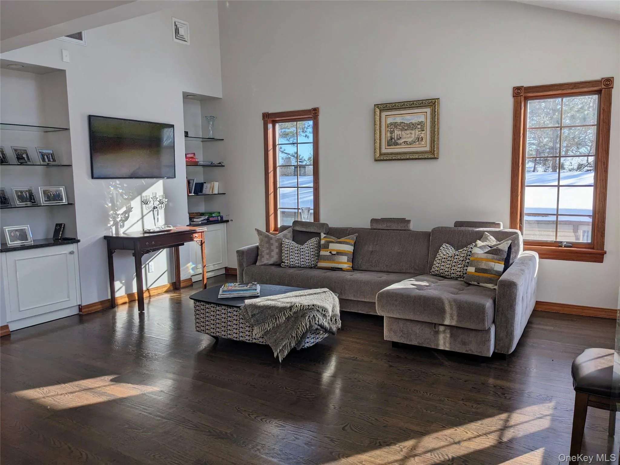 Living room featuring dark wood finished floors, high vaulted ceiling, and built in shelves Living room featuring dark wood finished floors, high vaulted ceiling, and built in shelves