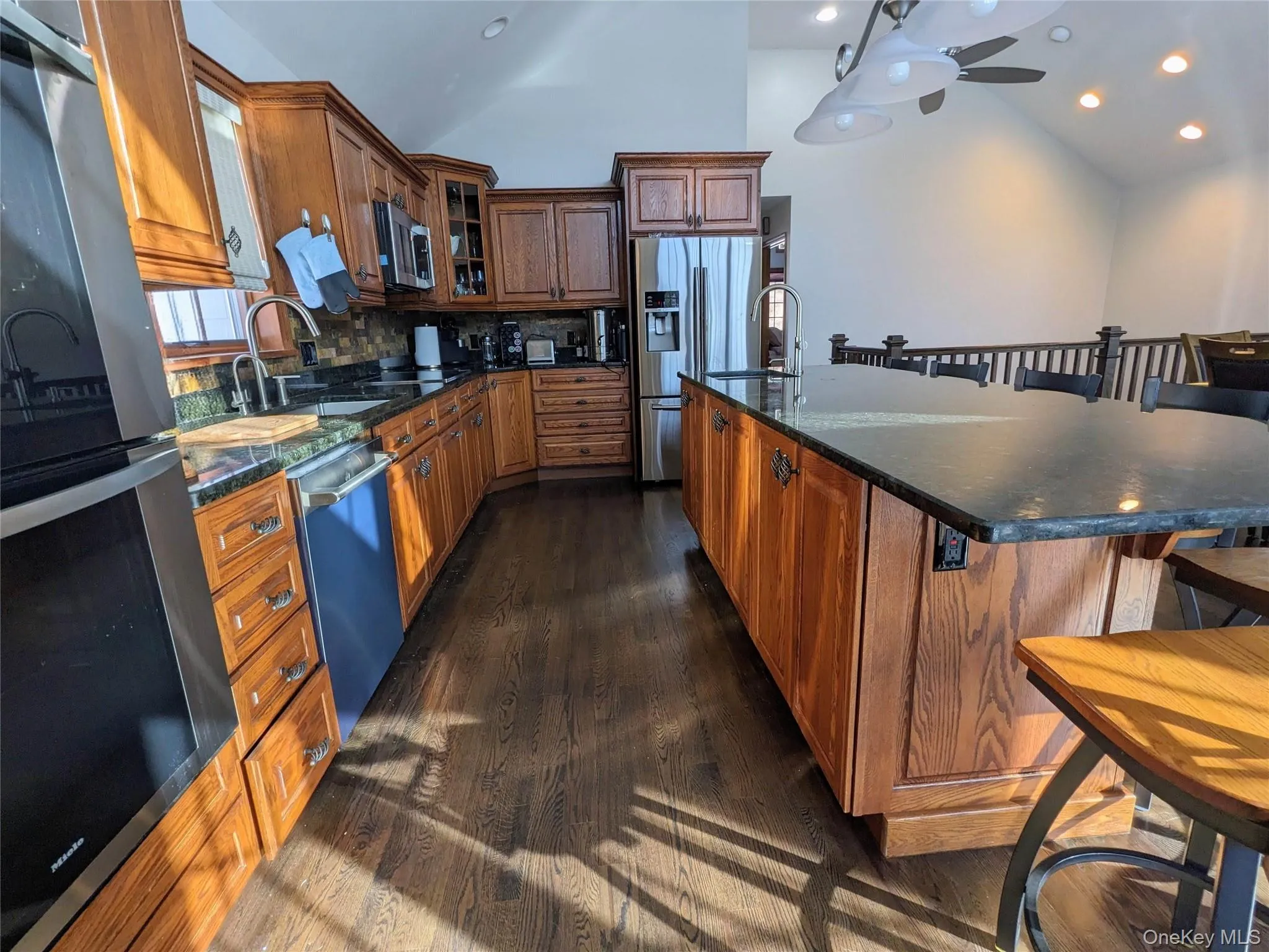 Kitchen with a kitchen bar, brown cabinetry, stainless steel appliances, lofted ceiling, and glass insert cabinets Kitchen with a kitchen bar, brown cabinetry, stainless steel appliances, lofted ceiling, and glass insert cabinets