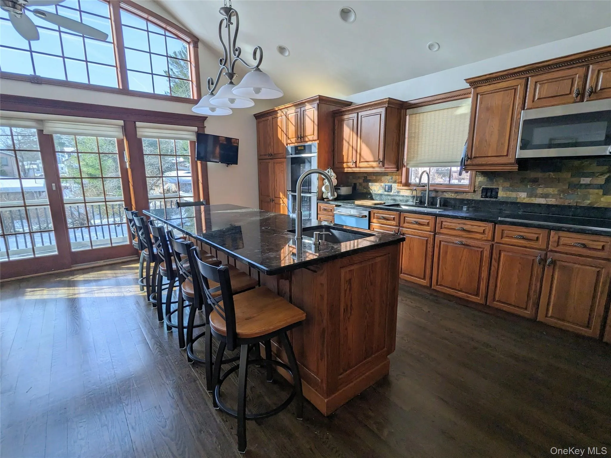 Kitchen with brown cabinetry, pendant lighting, stainless steel appliances, tasteful backsplash, and an island with sink Kitchen with brown cabinetry, pendant lighting, stainless steel appliances, tasteful backsplash, and an island with sink