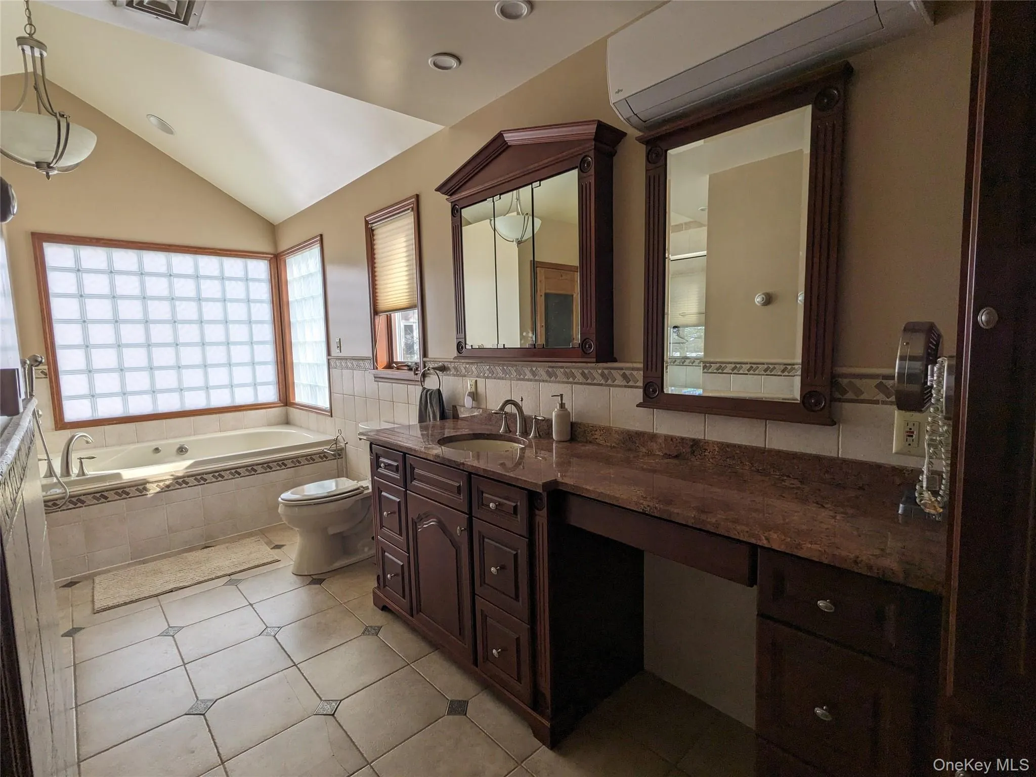Bathroom with a wall mounted AC, lofted ceiling, a garden tub, vanity, and light tile patterned floors Bathroom with a wall mounted AC, lofted ceiling, a garden tub, vanity, and light tile patterned floors