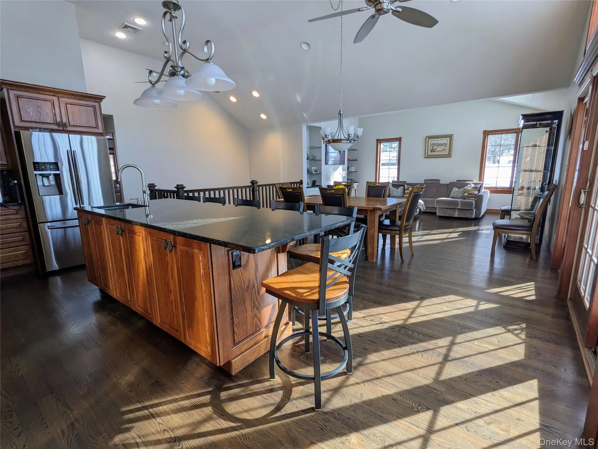 Kitchen featuring vaulted ceiling, open floor plan, a center island with sink, a kitchen breakfast bar, and stainless steel fridge Kitchen featuring vaulted ceiling, open floor plan, a center island with sink, a kitchen breakfast bar, and stainless steel fridge