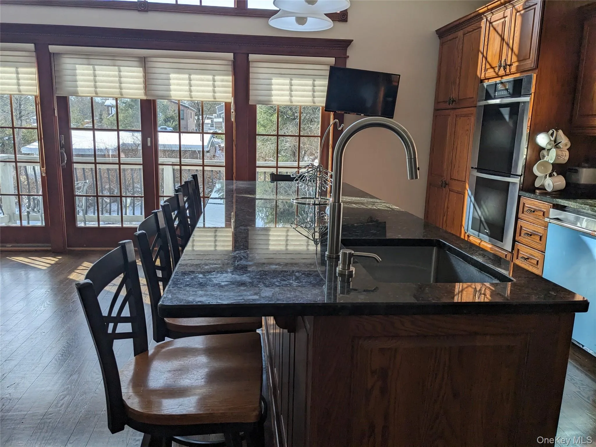 Kitchen with dark wood-style flooring, a kitchen island with sink, dark stone counters, a breakfast bar area, and stainless steel appliances Kitchen with dark wood-style flooring, a kitchen island with sink, dark stone counters, a breakfast bar area, and stainless steel appliances
