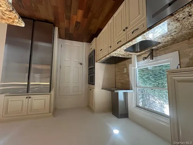 Kitchen with cream cabinets, fridge, light stone counters, range hood, and recessed lighting Kitchen with cream cabinets, fridge, light stone counters, range hood, and recessed lighting
