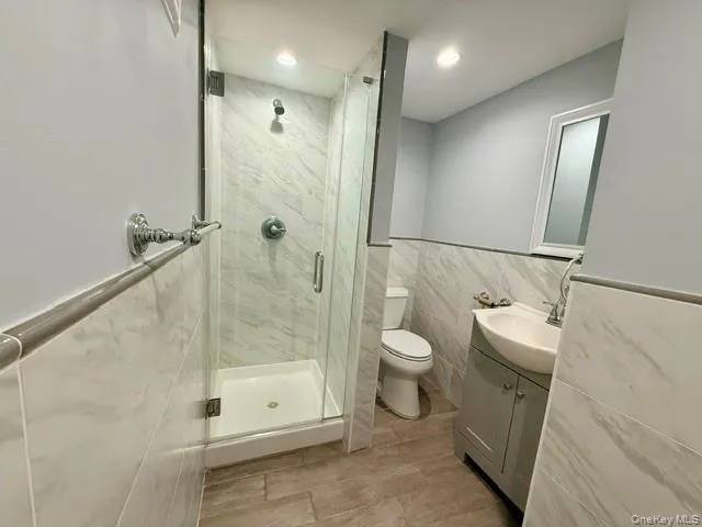 Bathroom with tile walls, wainscoting, vanity, a marble finish shower, and recessed lighting Bathroom with tile walls, wainscoting, vanity, a marble finish shower, and recessed lighting