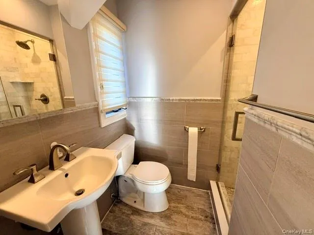 Full bathroom with a shower stall, wainscoting, and tile walls Full bathroom with a shower stall, wainscoting, and tile walls