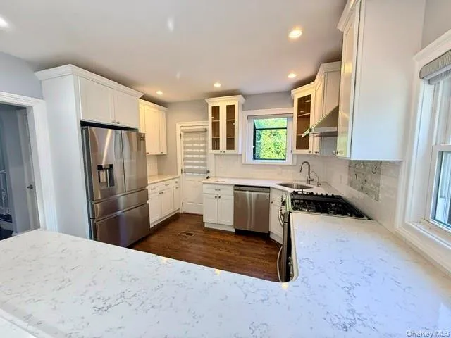 Kitchen with appliances with stainless steel finishes, glass insert cabinets, white cabinets, exhaust hood, and light stone countertops Kitchen with appliances with stainless steel finishes, glass insert cabinets, white cabinets, exhaust hood, and light stone countertops