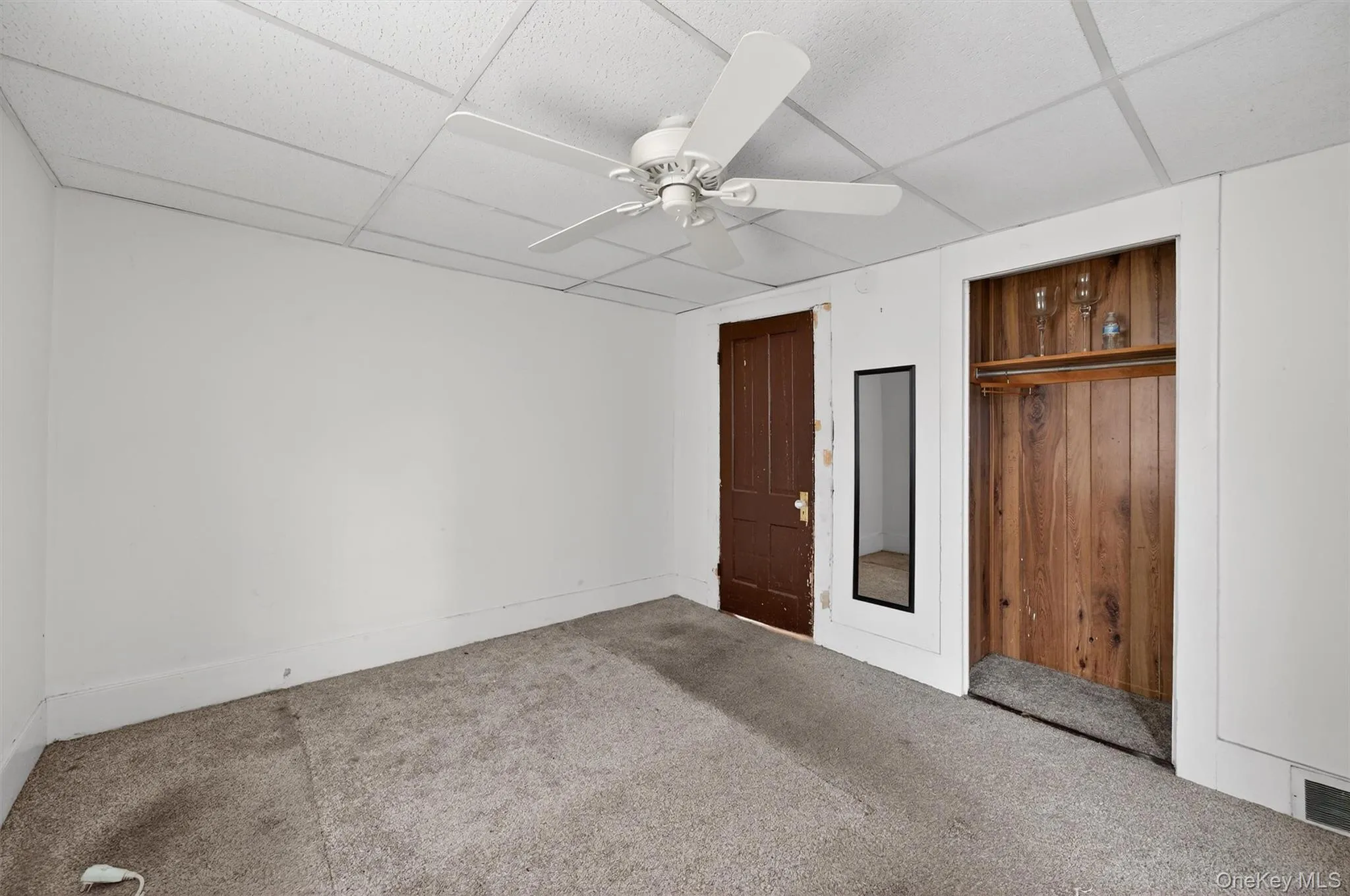 Unfurnished bedroom with a ceiling fan, carpet floors, a drop ceiling, and a closet Unfurnished bedroom with a ceiling fan, carpet floors, a drop ceiling, and a closet