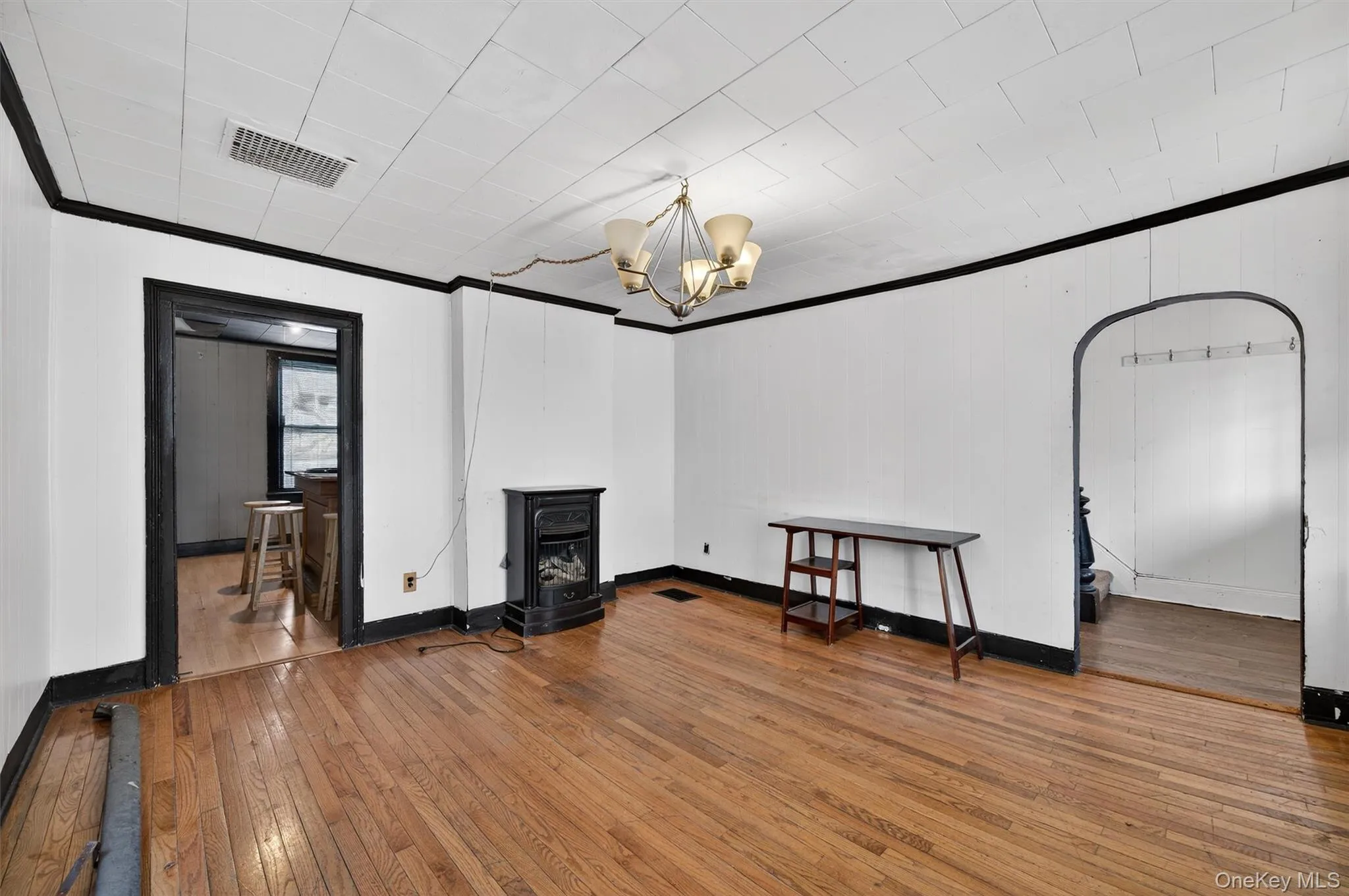 Living area featuring a wood stove, hardwood / wood-style flooring, ornamental molding, and a chandelier Living area featuring a wood stove, hardwood / wood-style flooring, ornamental molding, and a chandelier
