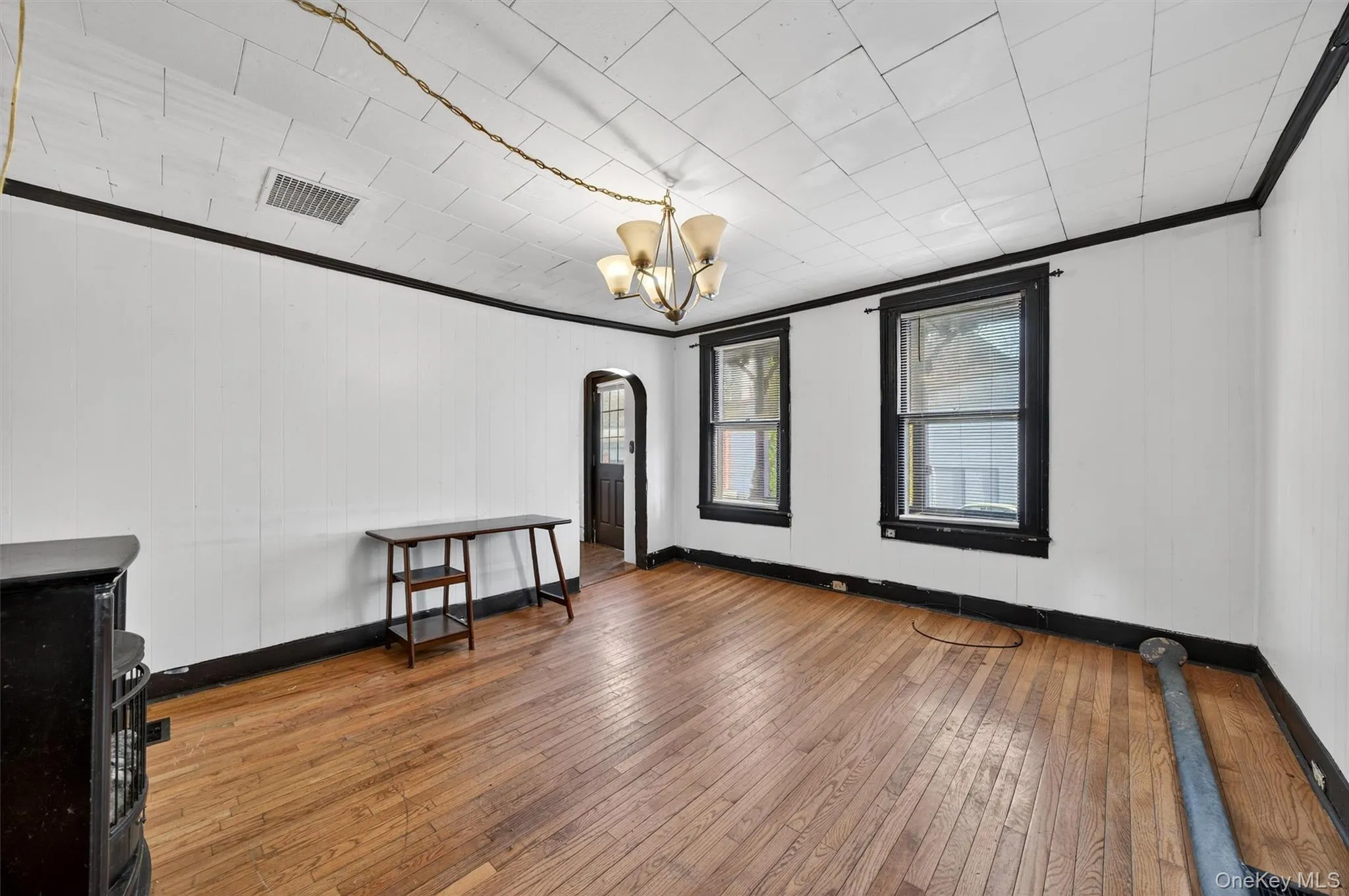 Empty room with arched walkways, hardwood / wood-style flooring, a chandelier, crown molding, and wooden walls Empty room with arched walkways, hardwood / wood-style flooring, a chandelier, crown molding, and wooden walls