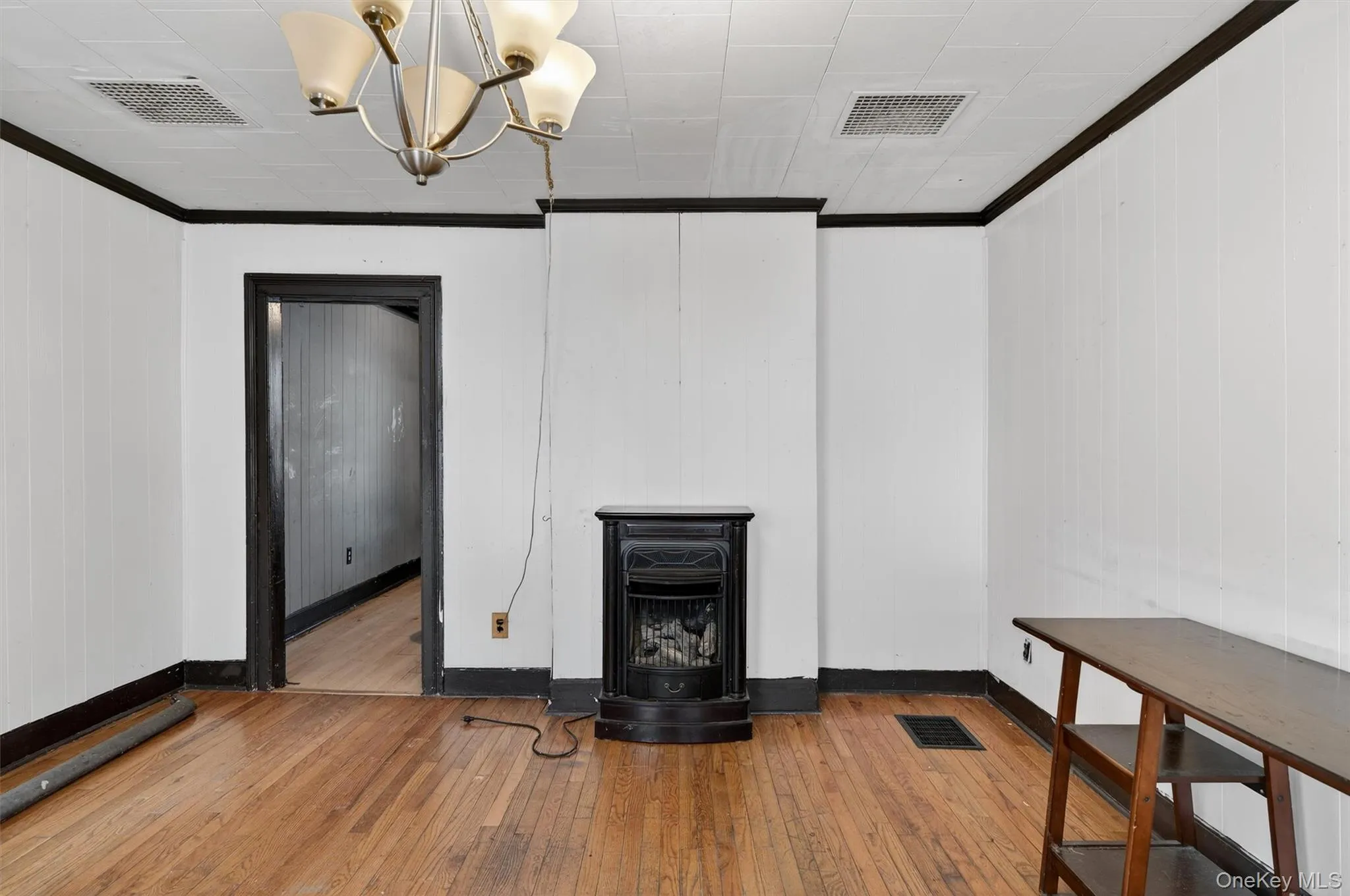 Unfurnished living room featuring a wood stove, hardwood / wood-style floors, a chandelier, crown molding, and wood walls Unfurnished living room featuring a wood stove, hardwood / wood-style floors, a chandelier, crown molding, and wood walls