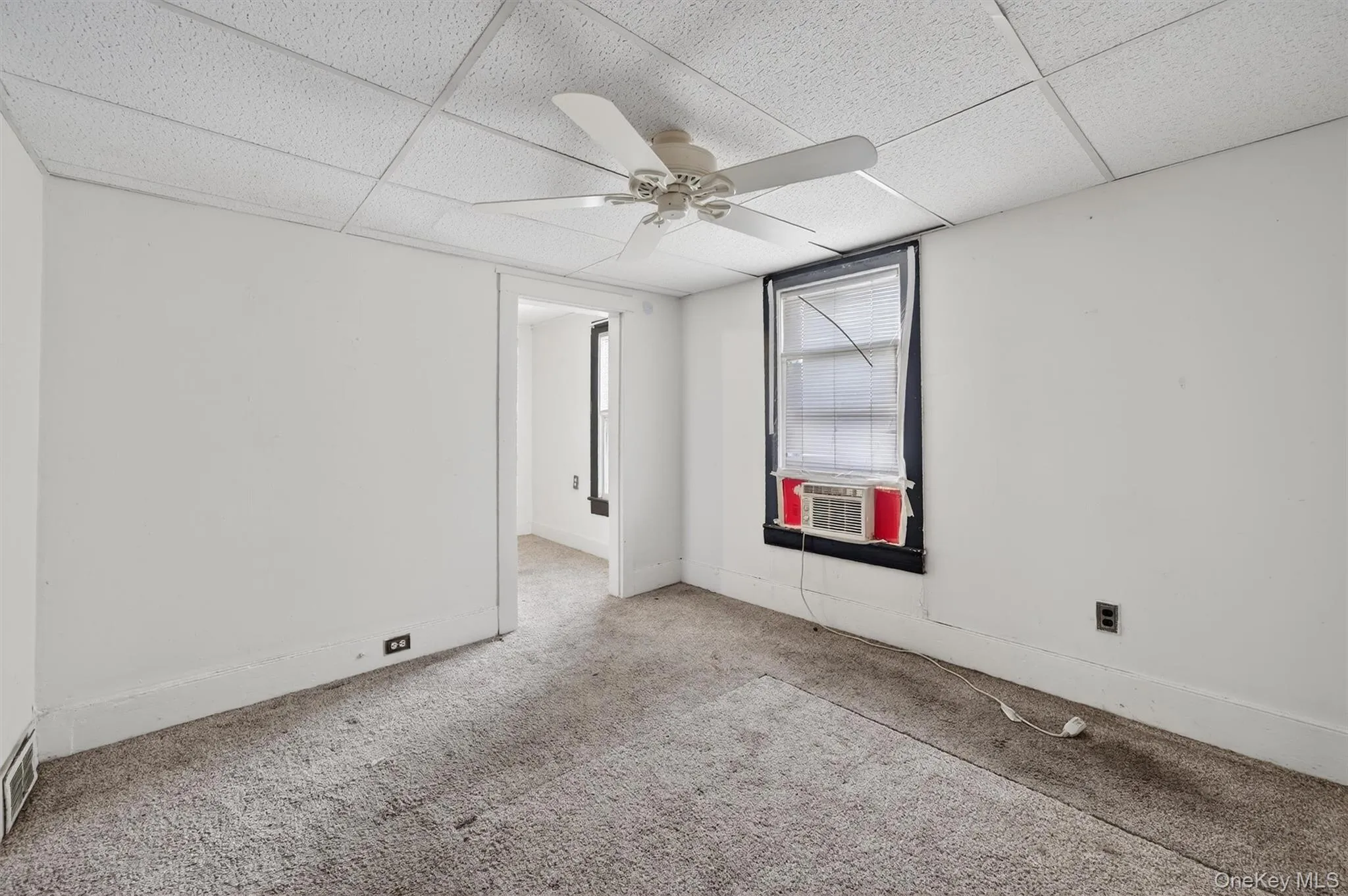 Carpeted empty room featuring a ceiling fan and a paneled ceiling Carpeted empty room featuring a ceiling fan and a paneled ceiling