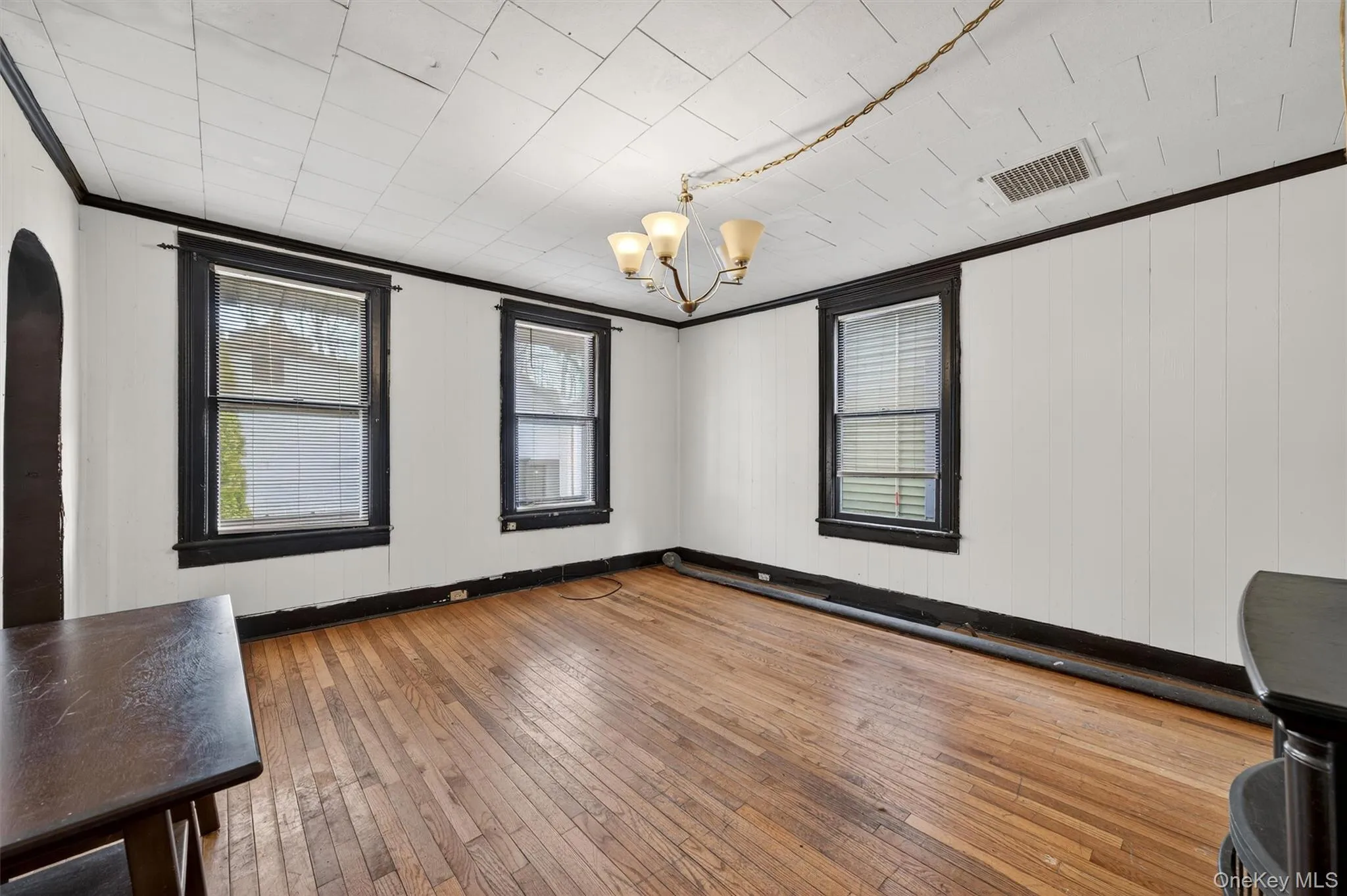 Spare room featuring ornamental molding, wood-type flooring, a chandelier, and wooden walls Spare room featuring ornamental molding, wood-type flooring, a chandelier, and wooden walls