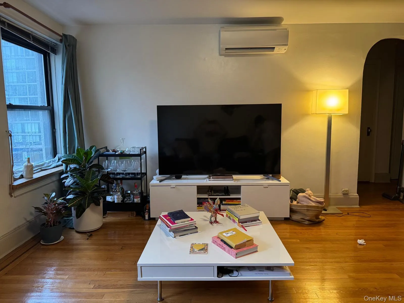 Living room featuring arched walkways, a wall mounted AC, light wood-style floors, and an office area Living room featuring arched walkways, a wall mounted AC, light wood-style floors, and an office area