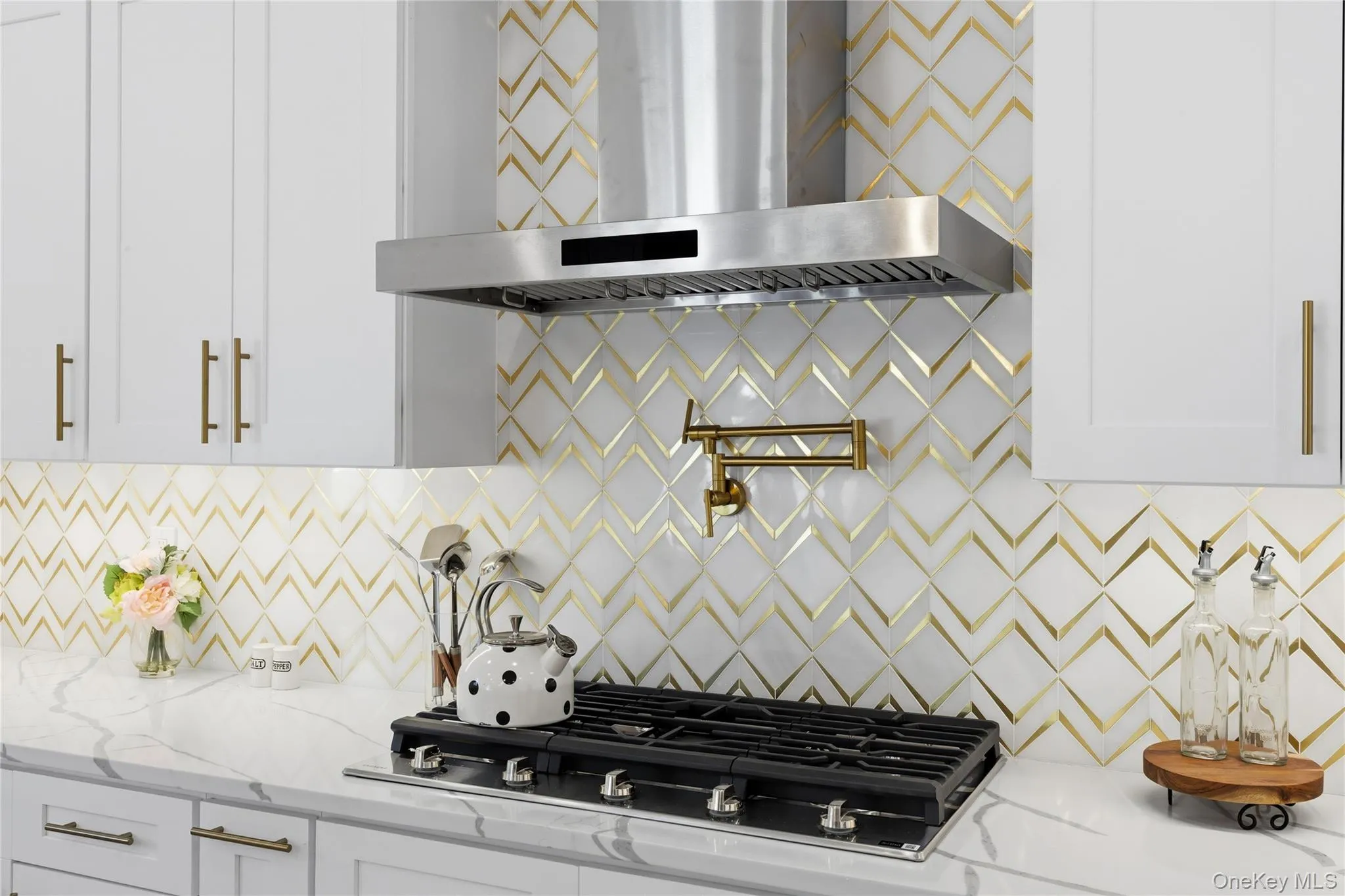 Kitchen with wall chimney exhaust hood, light stone counters, gas cooktop, backsplash, and white cabinetry Kitchen with wall chimney exhaust hood, light stone counters, gas cooktop, backsplash, and white cabinetry