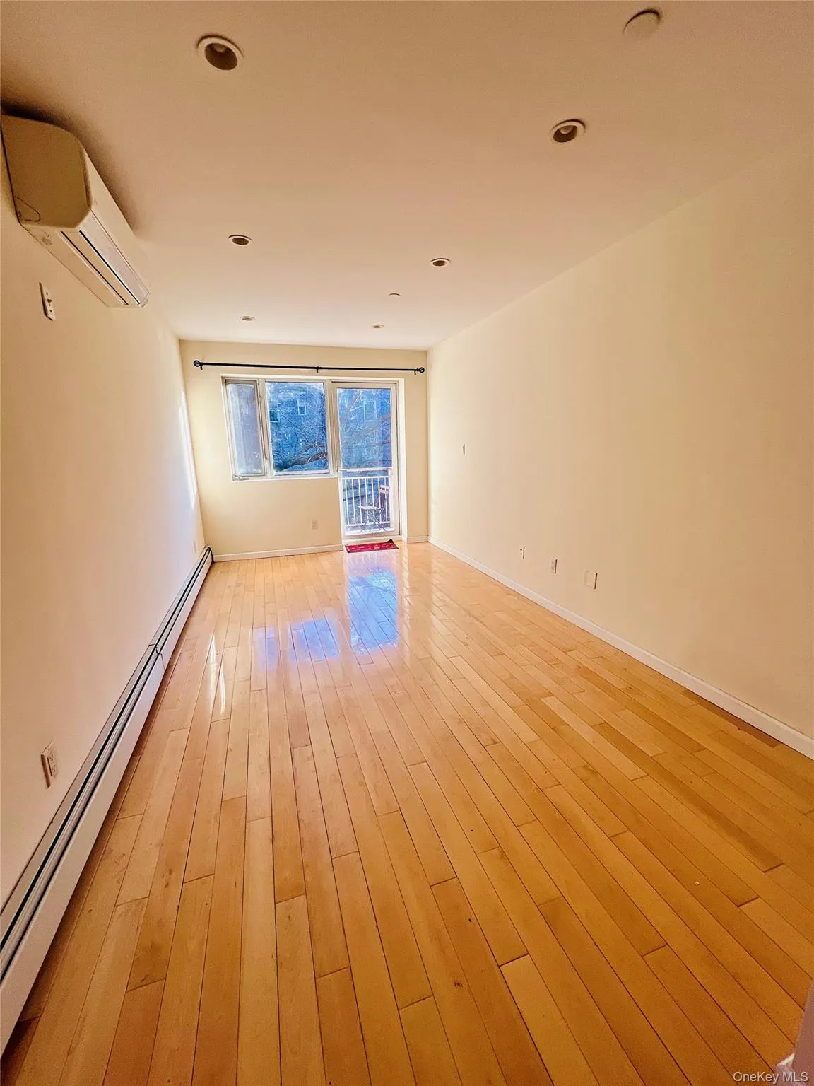 Empty room with baseboard heating, an AC wall unit, light wood finished floors, and recessed lighting Empty room with baseboard heating, an AC wall unit, light wood finished floors, and recessed lighting