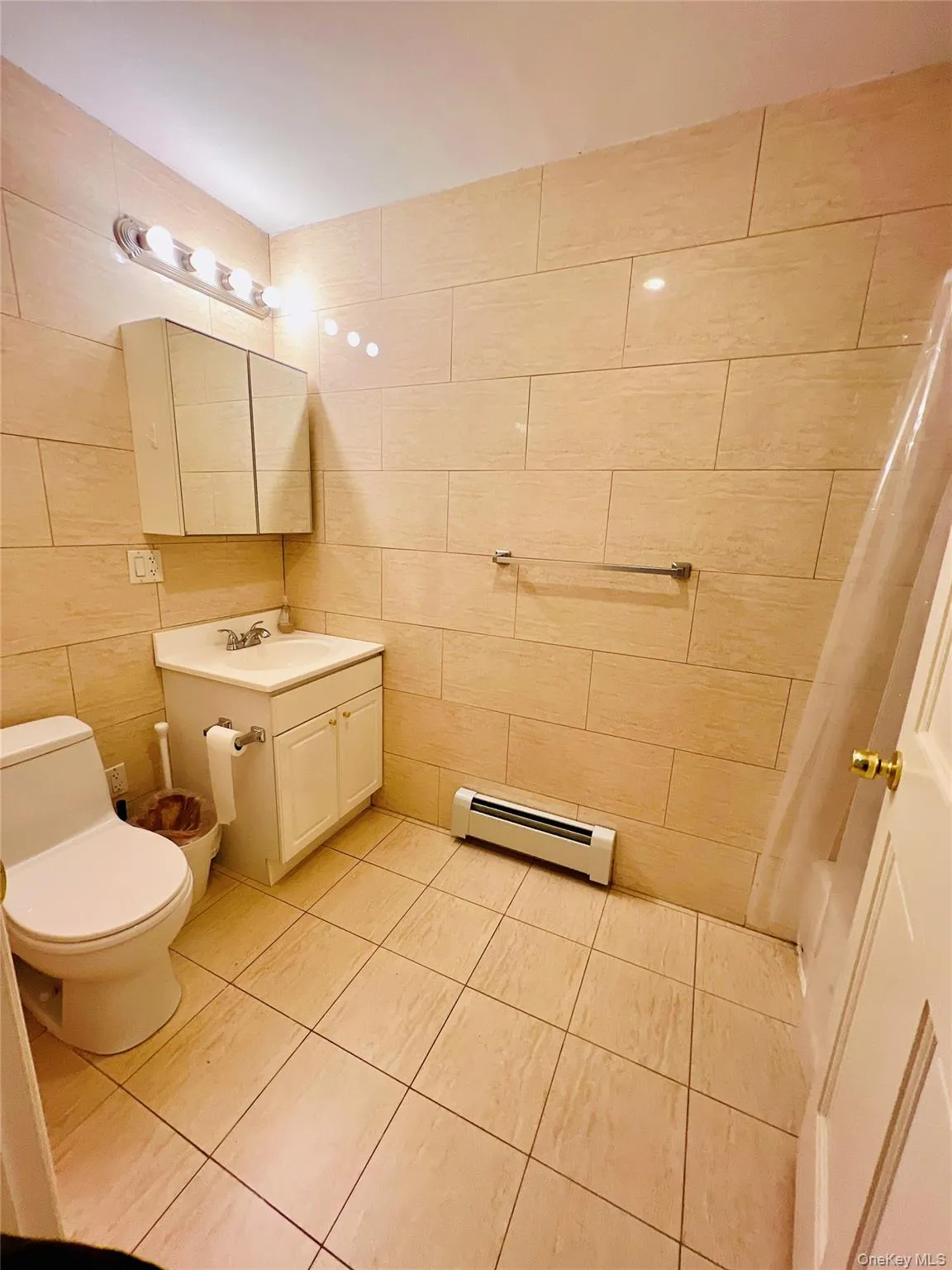 Full bath featuring vanity, baseboard heating, light tile patterned floors, tile walls, and shower / bath combination with curtain Full bath featuring vanity, baseboard heating, light tile patterned floors, tile walls, and shower / bath combination with curtain