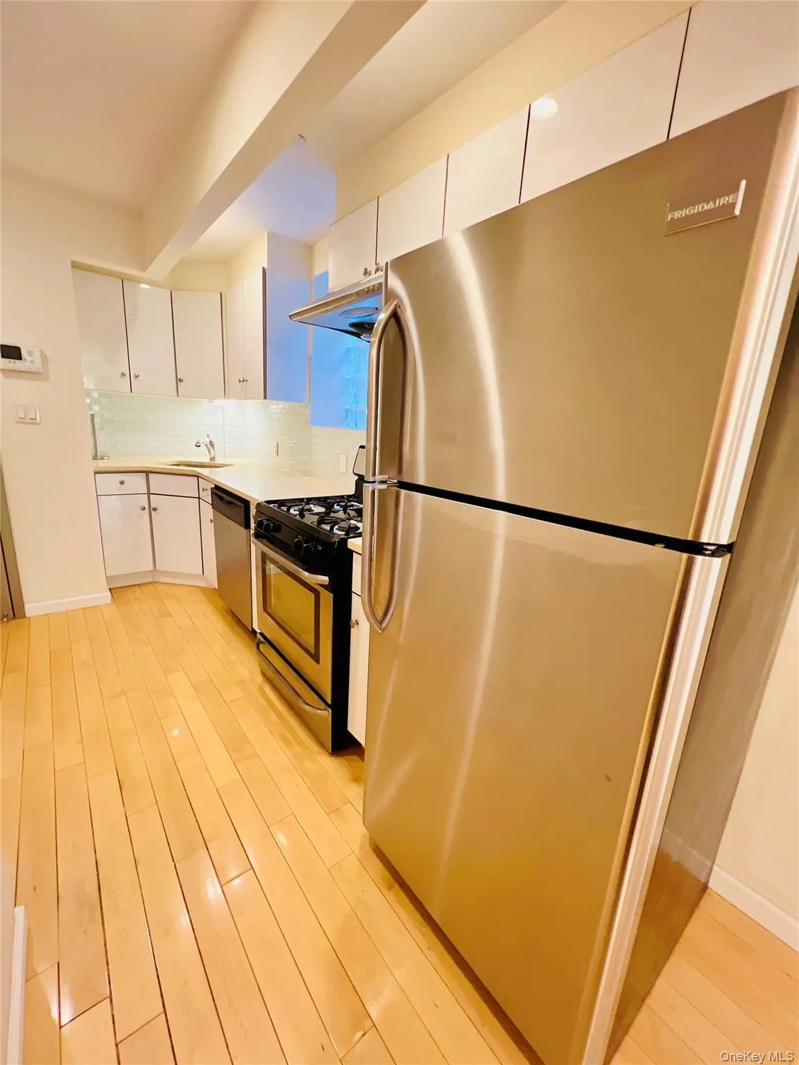 Kitchen featuring appliances with stainless steel finishes, white cabinetry, light countertops, and light wood finished floors Kitchen featuring appliances with stainless steel finishes, white cabinetry, light countertops, and light wood finished floors