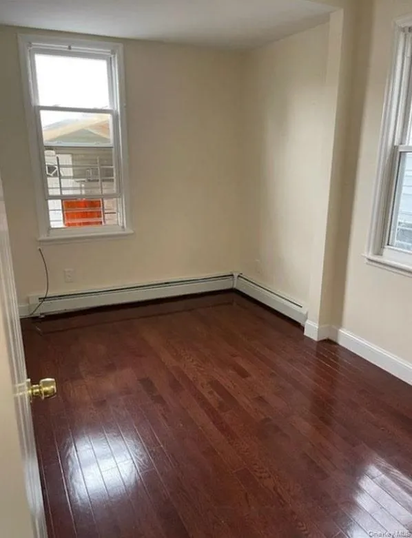 Empty room with dark wood-style flooring, plenty of natural light, and baseboard heating Empty room with dark wood-style flooring, plenty of natural light, and baseboard heating