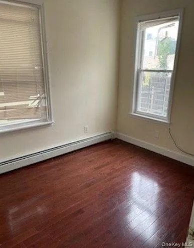 Empty room with baseboard heating and dark wood finished floors Empty room with baseboard heating and dark wood finished floors