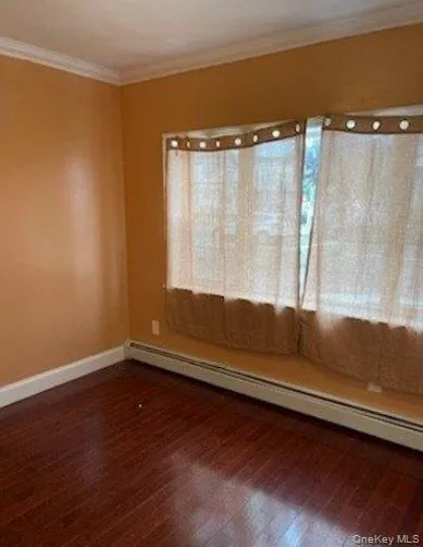 Unfurnished room featuring a baseboard heating unit, ornamental molding, and dark wood-style floors Unfurnished room featuring a baseboard heating unit, ornamental molding, and dark wood-style floors