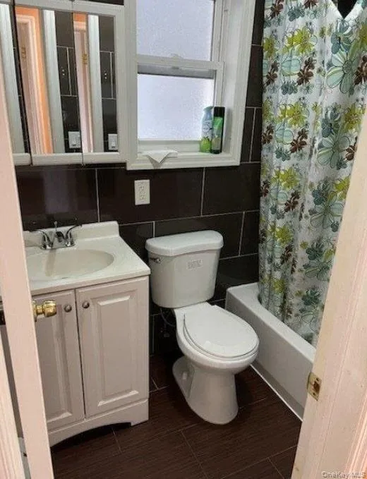 Bathroom featuring vanity, shower / bath combination with curtain, tile walls, and dark wood-style flooring Bathroom featuring vanity, shower / bath combination with curtain, tile walls, and dark wood-style flooring