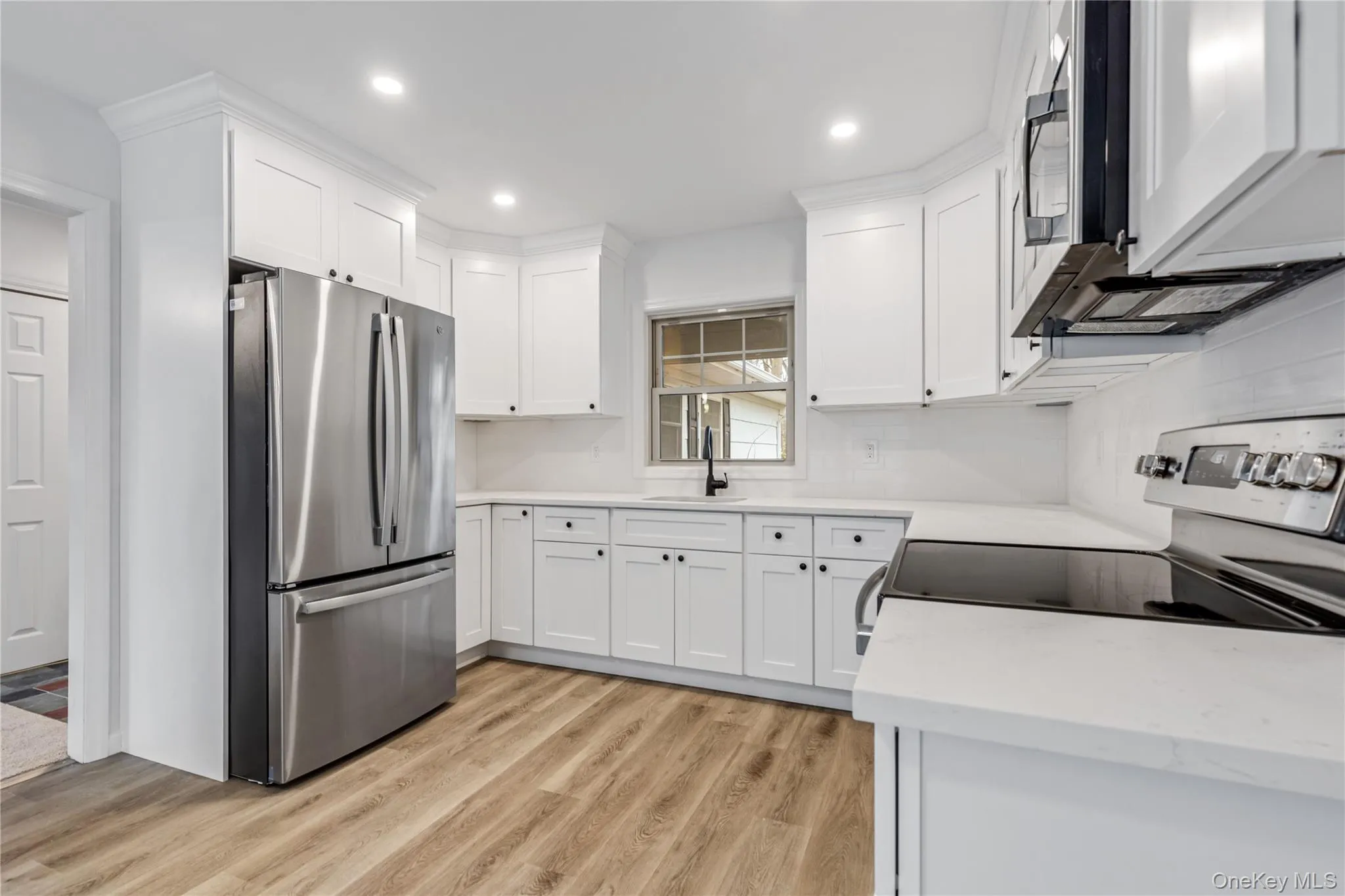 Kitchen with appliances with stainless steel finishes, white cabinets, light wood-style floors, light stone counters, and recessed lighting Kitchen with appliances with stainless steel finishes, white cabinets, light wood-style floors, light stone counters, and recessed lighting