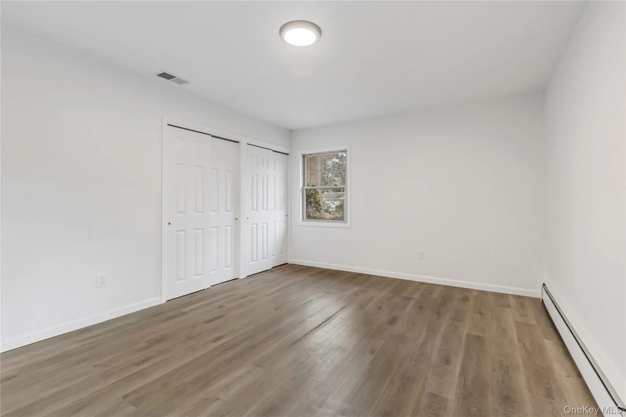 Unfurnished bedroom with a baseboard heating unit, multiple closets, and wood finished floors Unfurnished bedroom with a baseboard heating unit, multiple closets, and wood finished floors