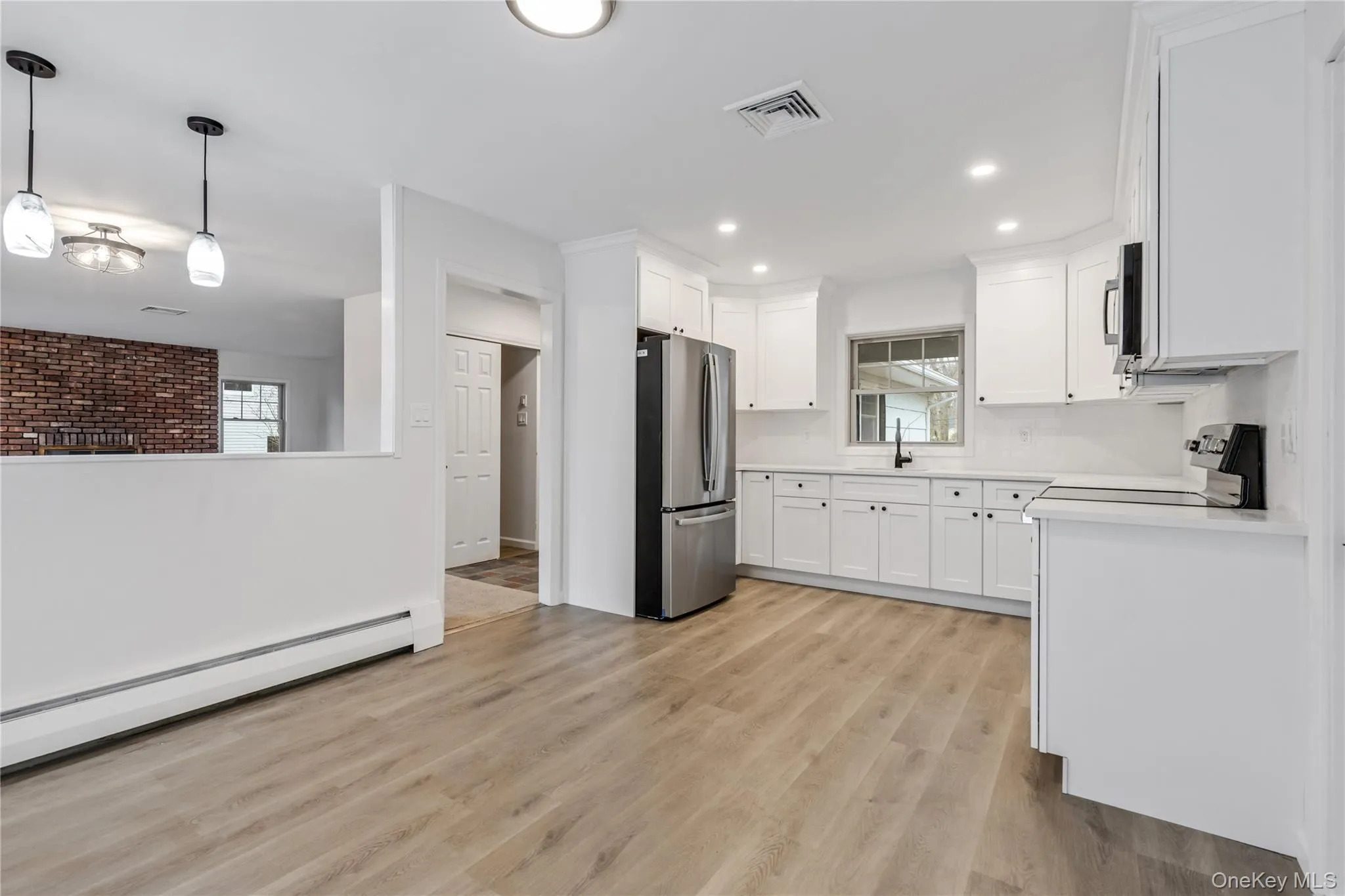 Kitchen with baseboard heating, white cabinetry, stainless steel appliances, and light wood-style floors Kitchen with baseboard heating, white cabinetry, stainless steel appliances, and light wood-style floors