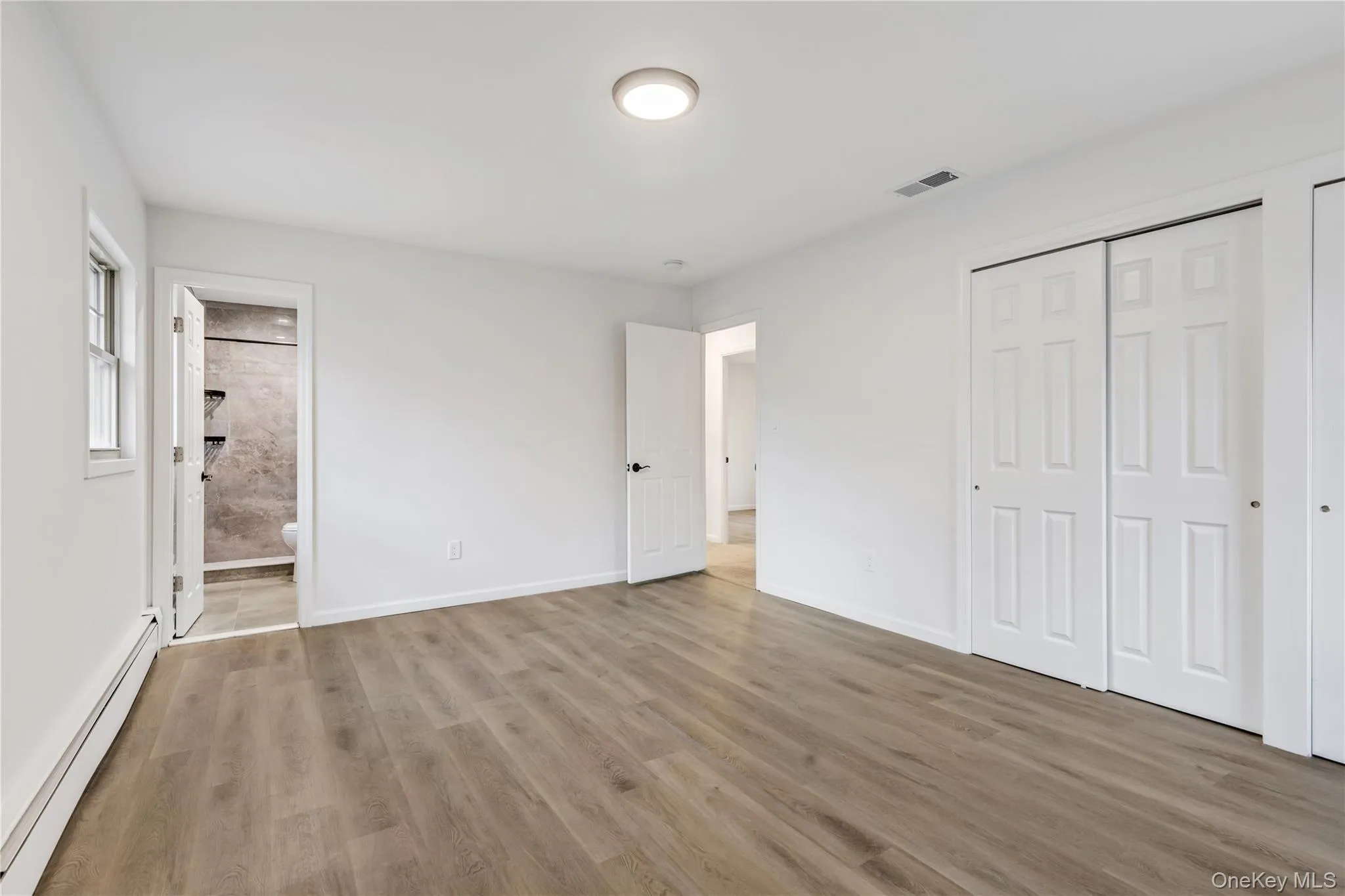Unfurnished bedroom featuring a baseboard heating unit, light wood-style floors, a closet, and ensuite bathroom Unfurnished bedroom featuring a baseboard heating unit, light wood-style floors, a closet, and ensuite bathroom