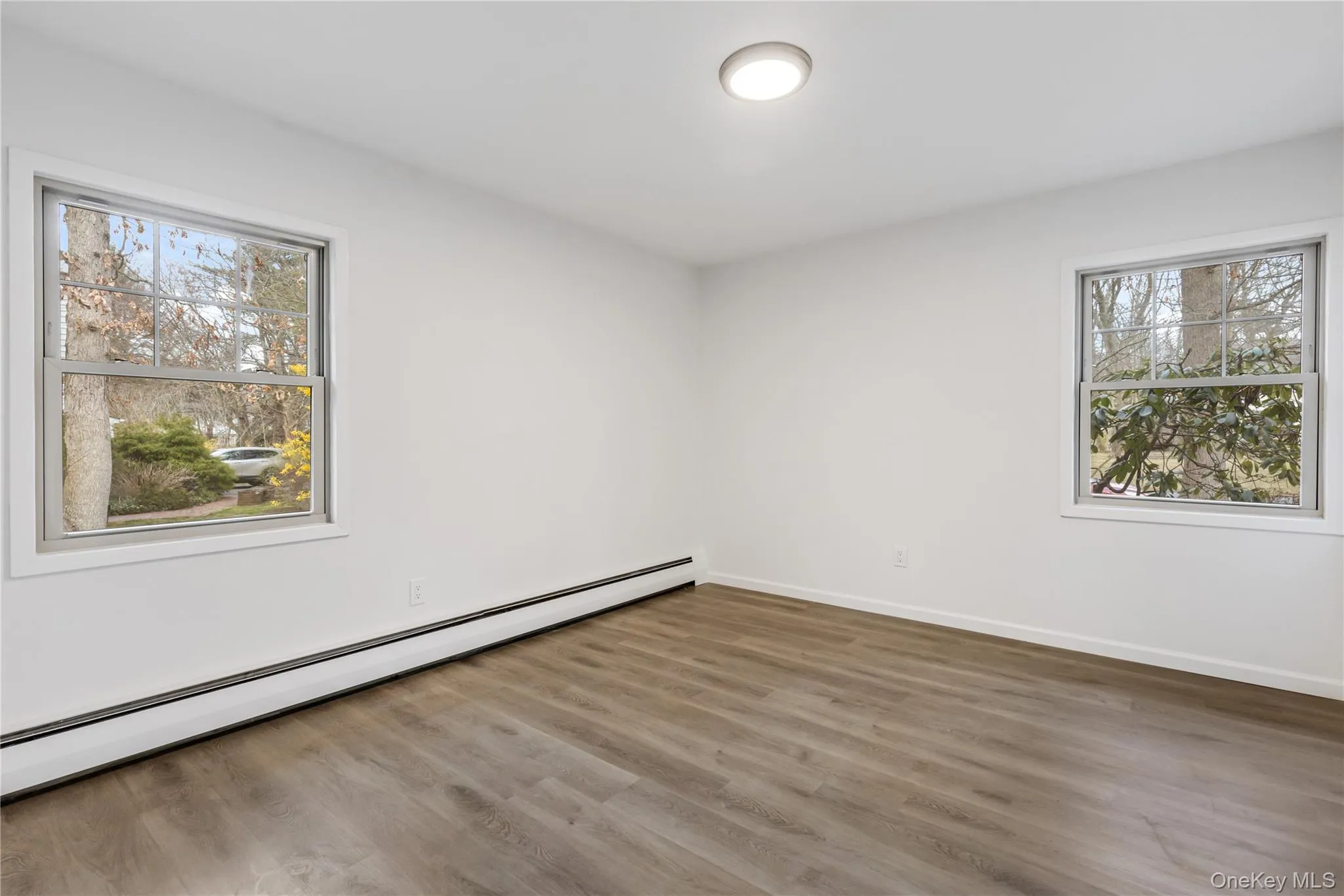 Empty room with baseboard heating, wood finished floors, and plenty of natural light Empty room with baseboard heating, wood finished floors, and plenty of natural light