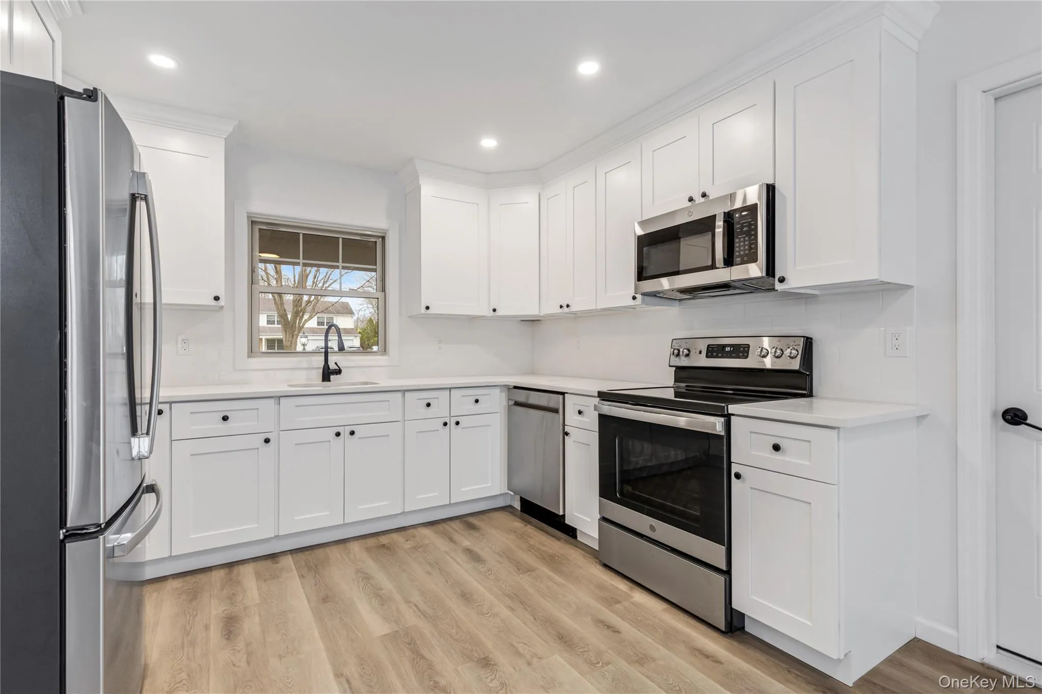 Kitchen with appliances with stainless steel finishes, white cabinets, light wood-type flooring, backsplash, and recessed lighting Kitchen with appliances with stainless steel finishes, white cabinets, light wood-type flooring, backsplash, and recessed lighting