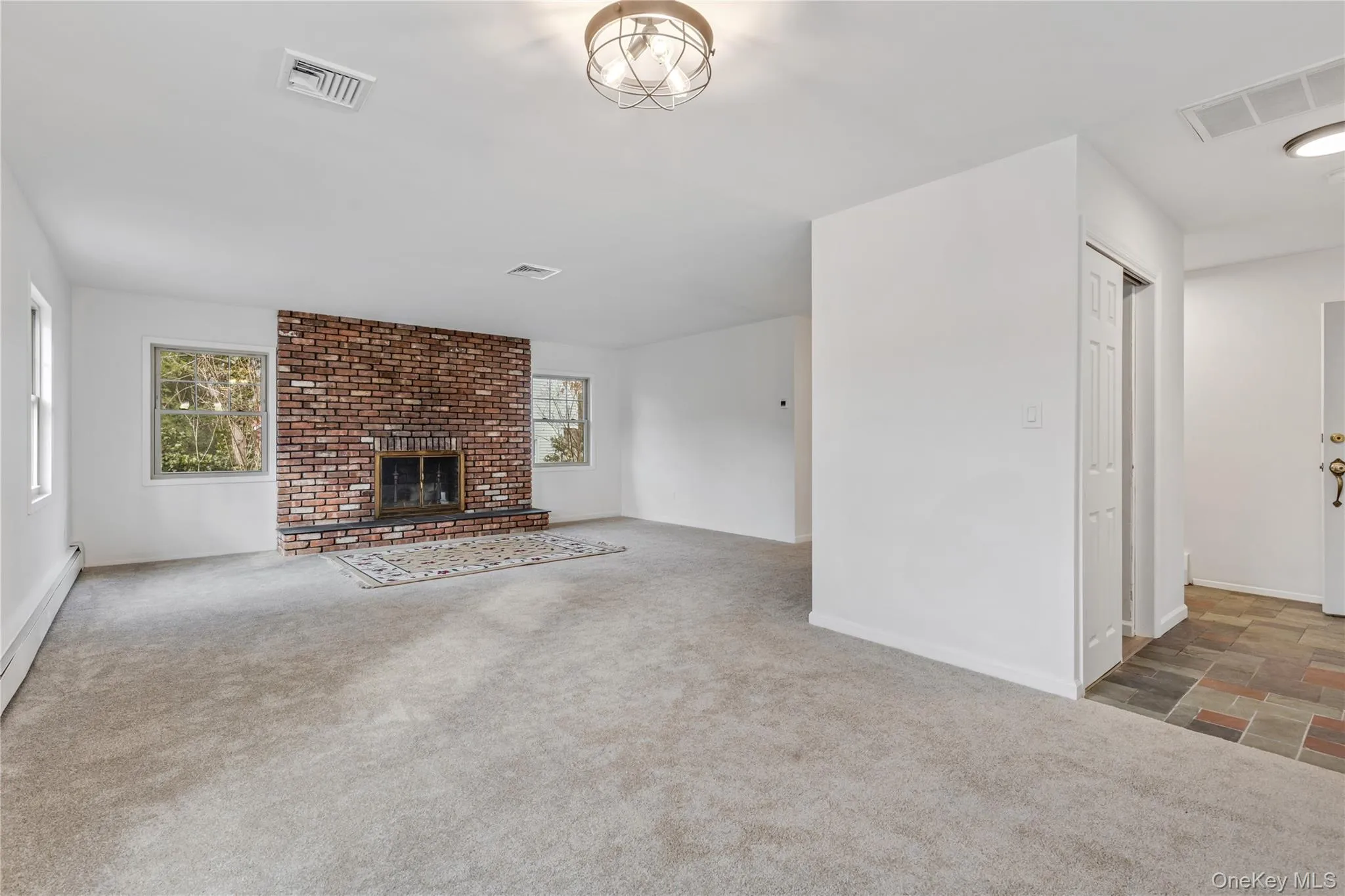 Unfurnished living room with carpet floors, a brick fireplace, and baseboard heating Unfurnished living room with carpet floors, a brick fireplace, and baseboard heating