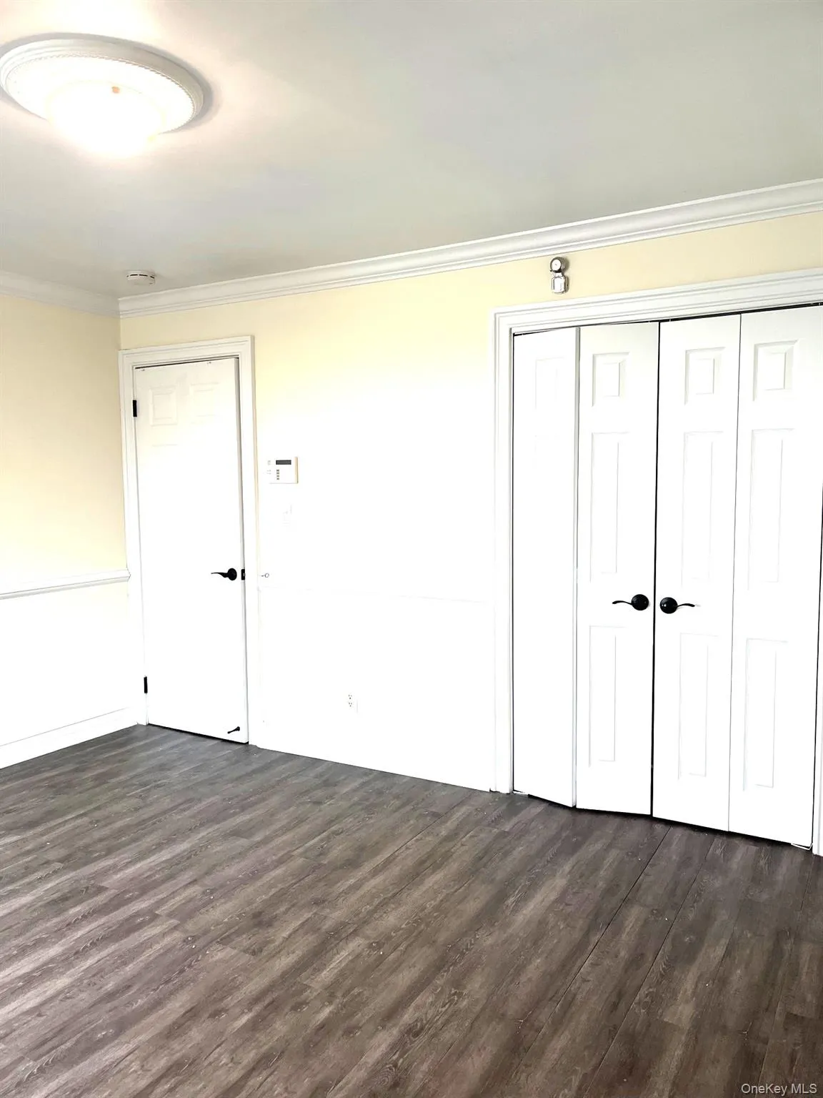 Unfurnished bedroom with dark wood-type flooring, ornamental molding, and a closet Unfurnished bedroom with dark wood-type flooring, ornamental molding, and a closet