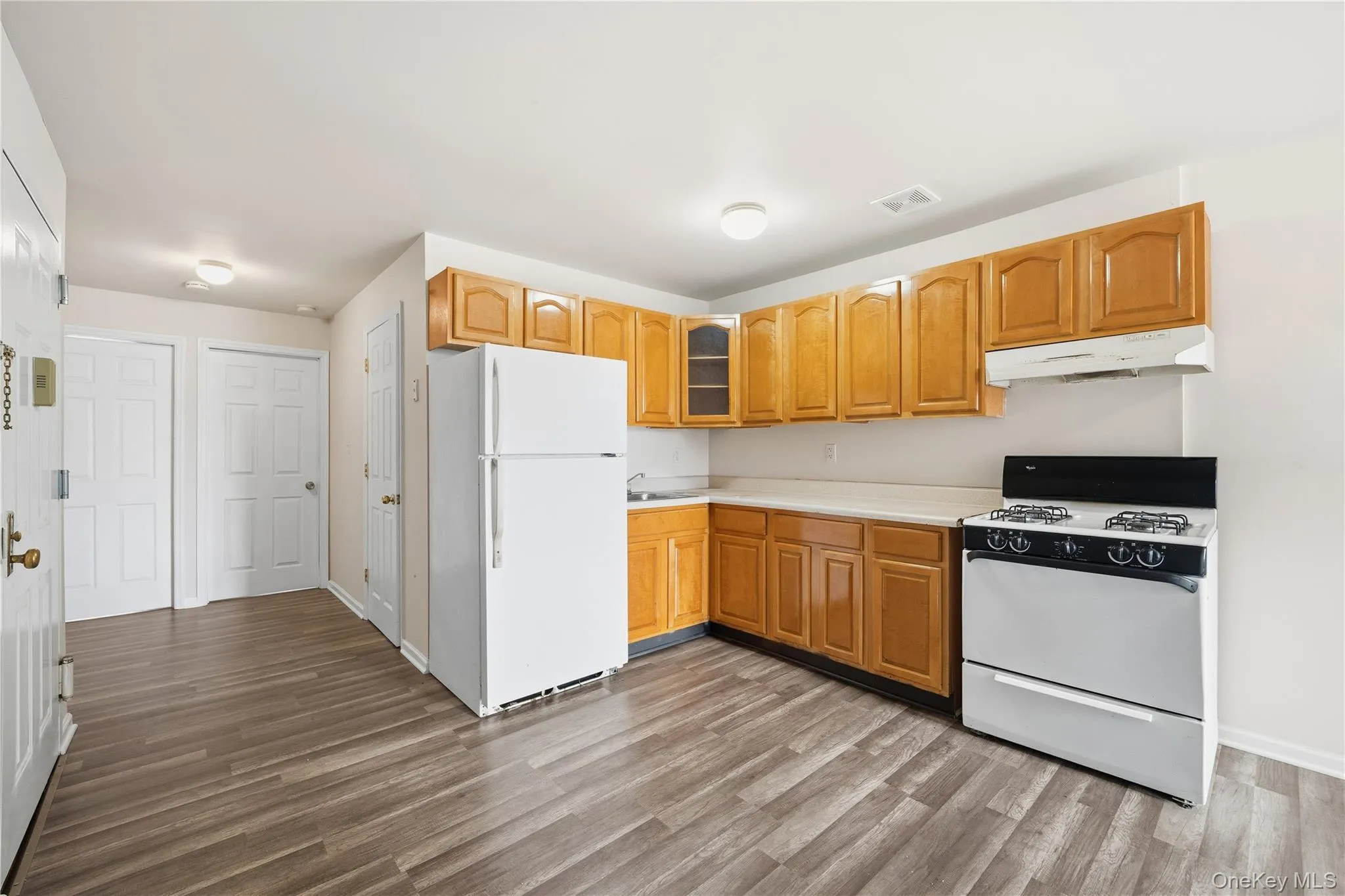 Kitchen featuring white appliances, light countertops, under cabinet range hood, glass insert cabinets, and light wood finished floors Kitchen featuring white appliances, light countertops, under cabinet range hood, glass insert cabinets, and light wood finished floors
